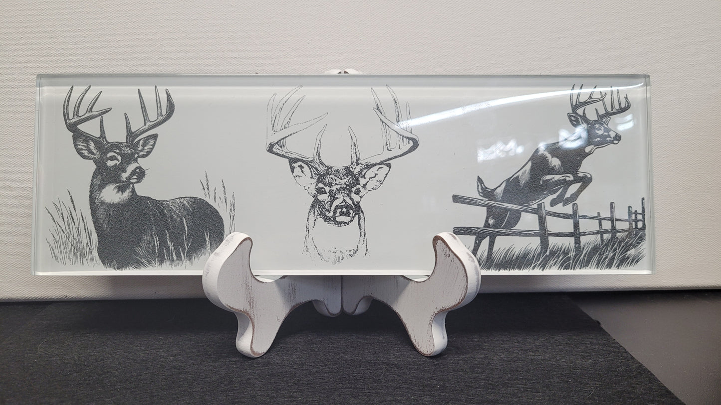 This basic glass wall tile as been transformed into a beautiful laser engraved whitetail buck collage image. The fine detail from the laser really shines through on the white background. Measuring 4" tall x 12" wide and 1/4" thick, this tile is a strong sturdy piece. Black felt backing allows you to display flat on a table or use the white washed wooden easel that comes with it.