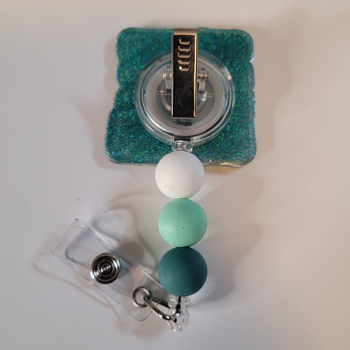 Green and white beaded badge holder with a clear plastic clip on a light gray background