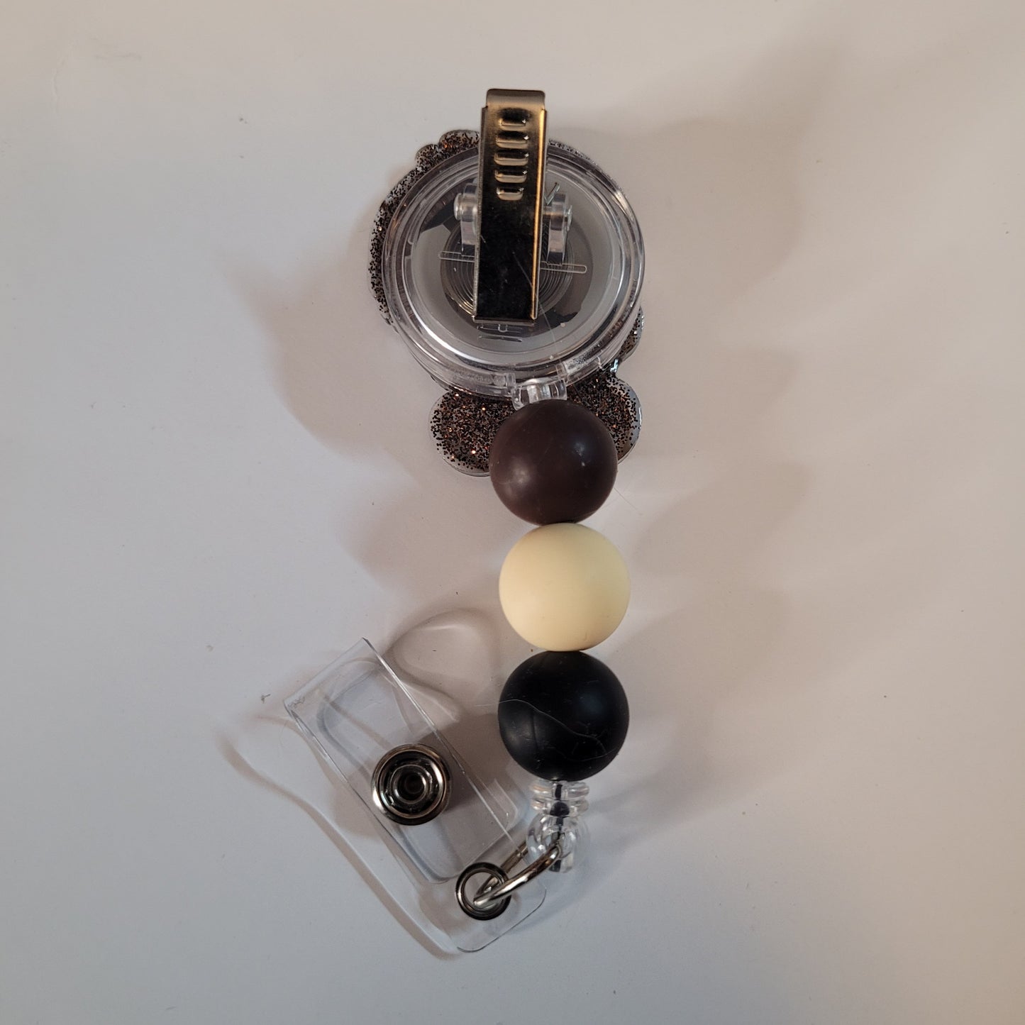 Clear badge holder with brown, black, and white beads on a light gray background