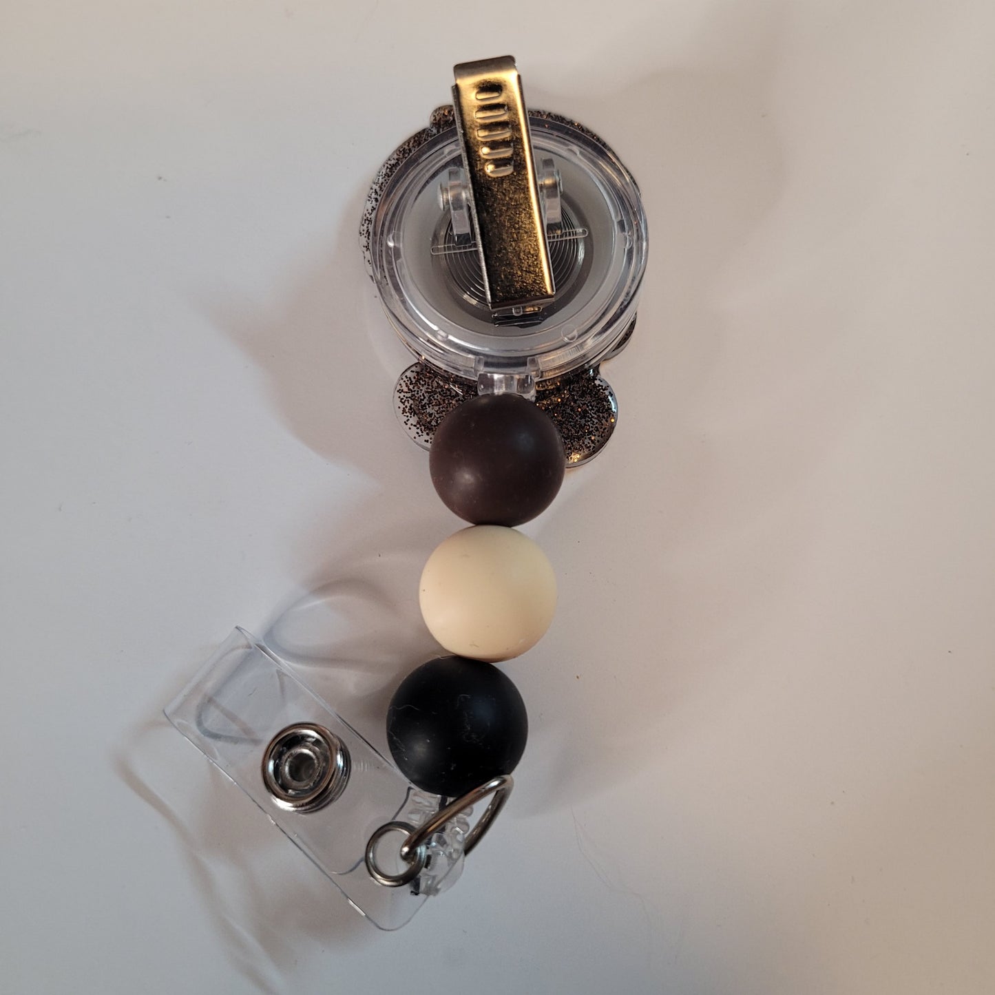 Retractable badge holder with black, white, and gold accents on a light gray background