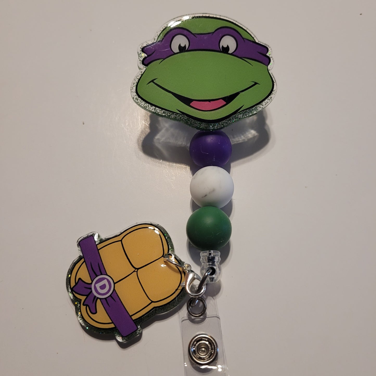 Character-themed badge holder with green face and purple accents on a white background