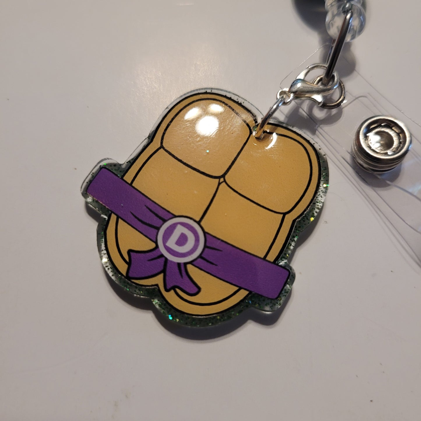 Tortoise shell badge holder with purple belt and letter 'D' on a white background