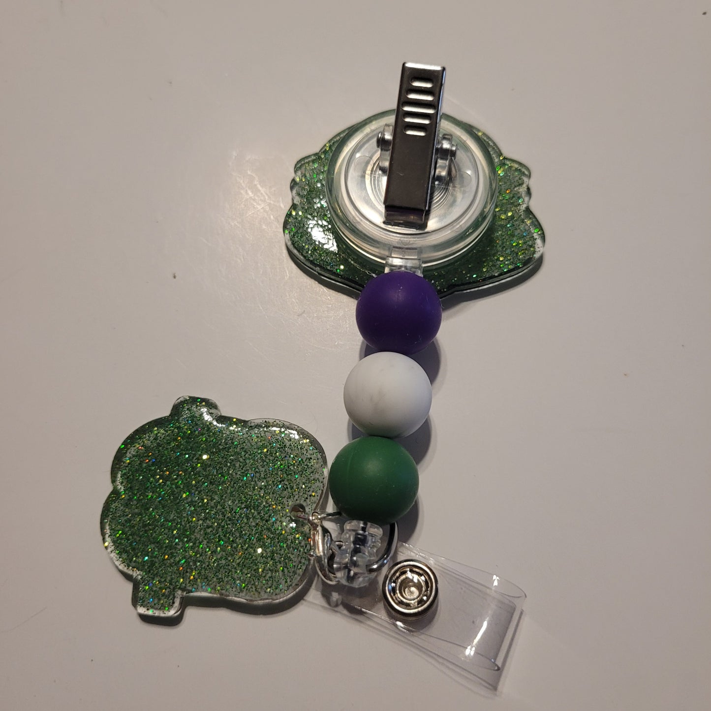 Retractable badge holder with green, white, and purple beads on a white background