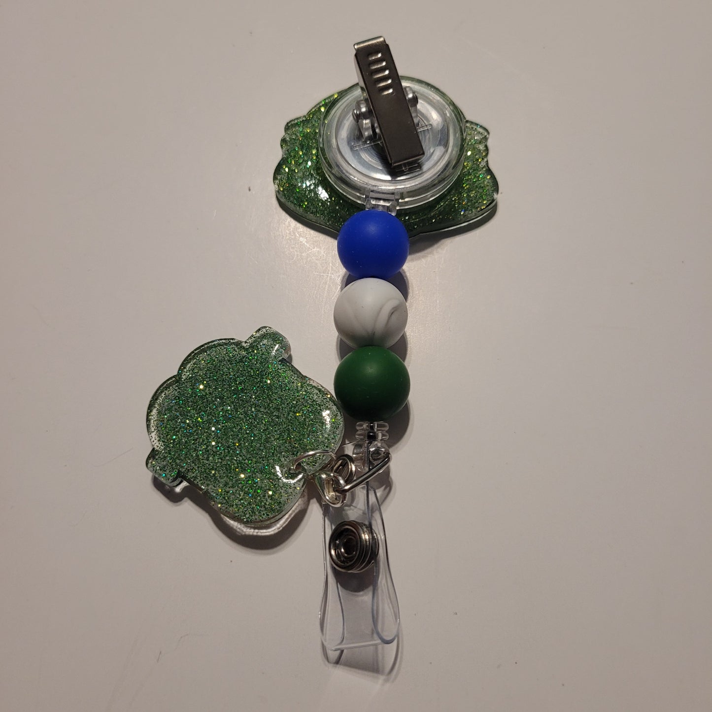 Retractable badge holder with green, blue, and white balls on a beige background