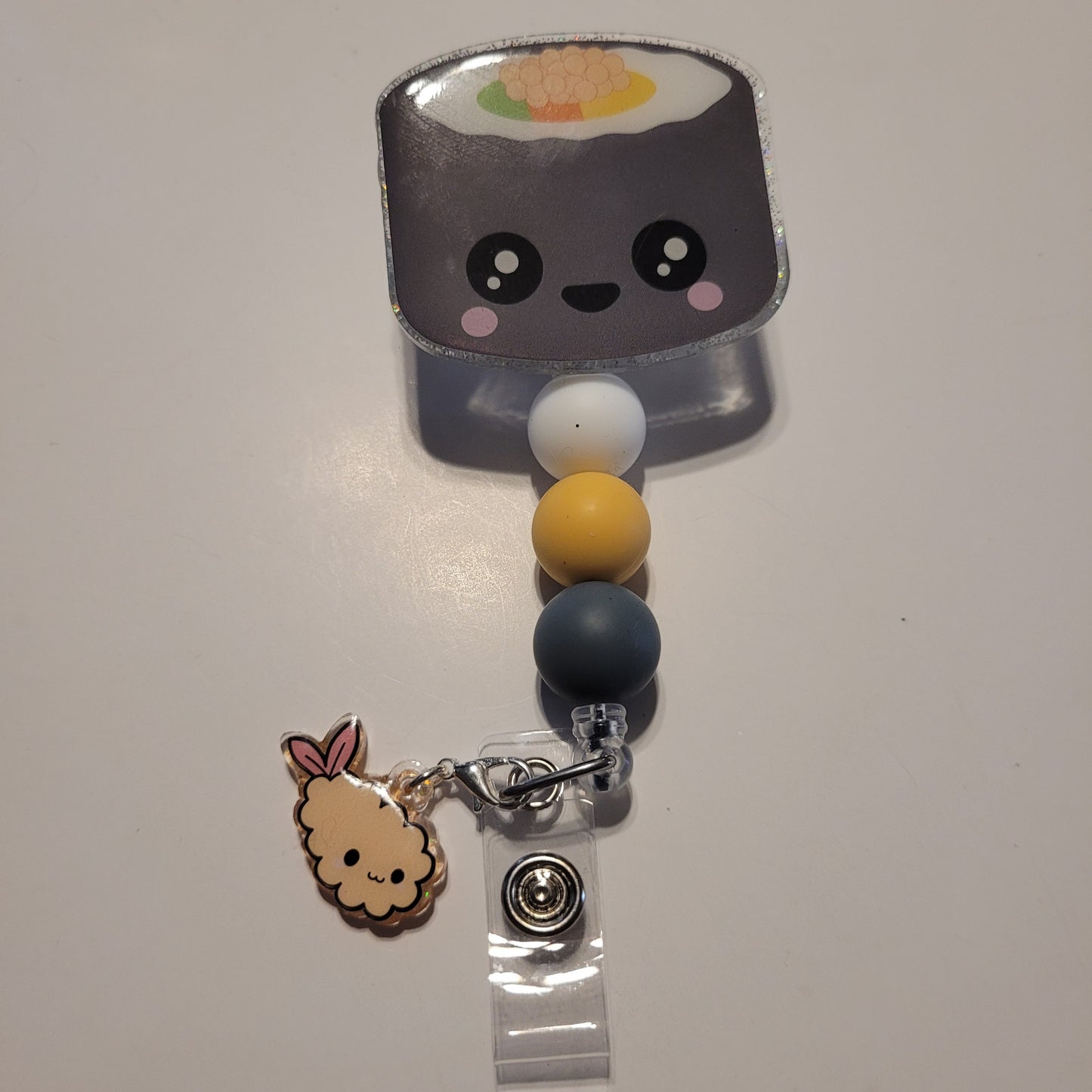 Kawaii-style sushi-themed badge holder with colorful beads on a plain background