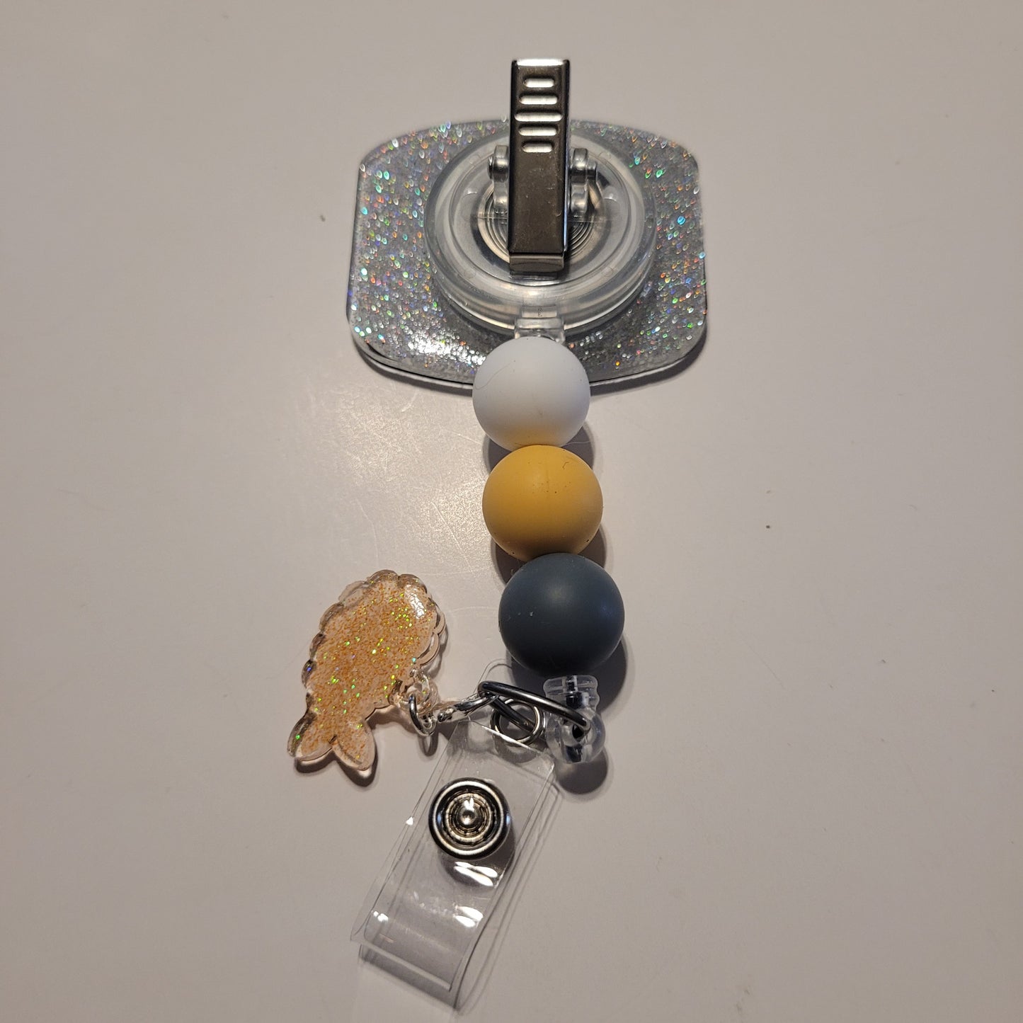 Retractable badge holder with colorful beads and a fish charm on a light gray background