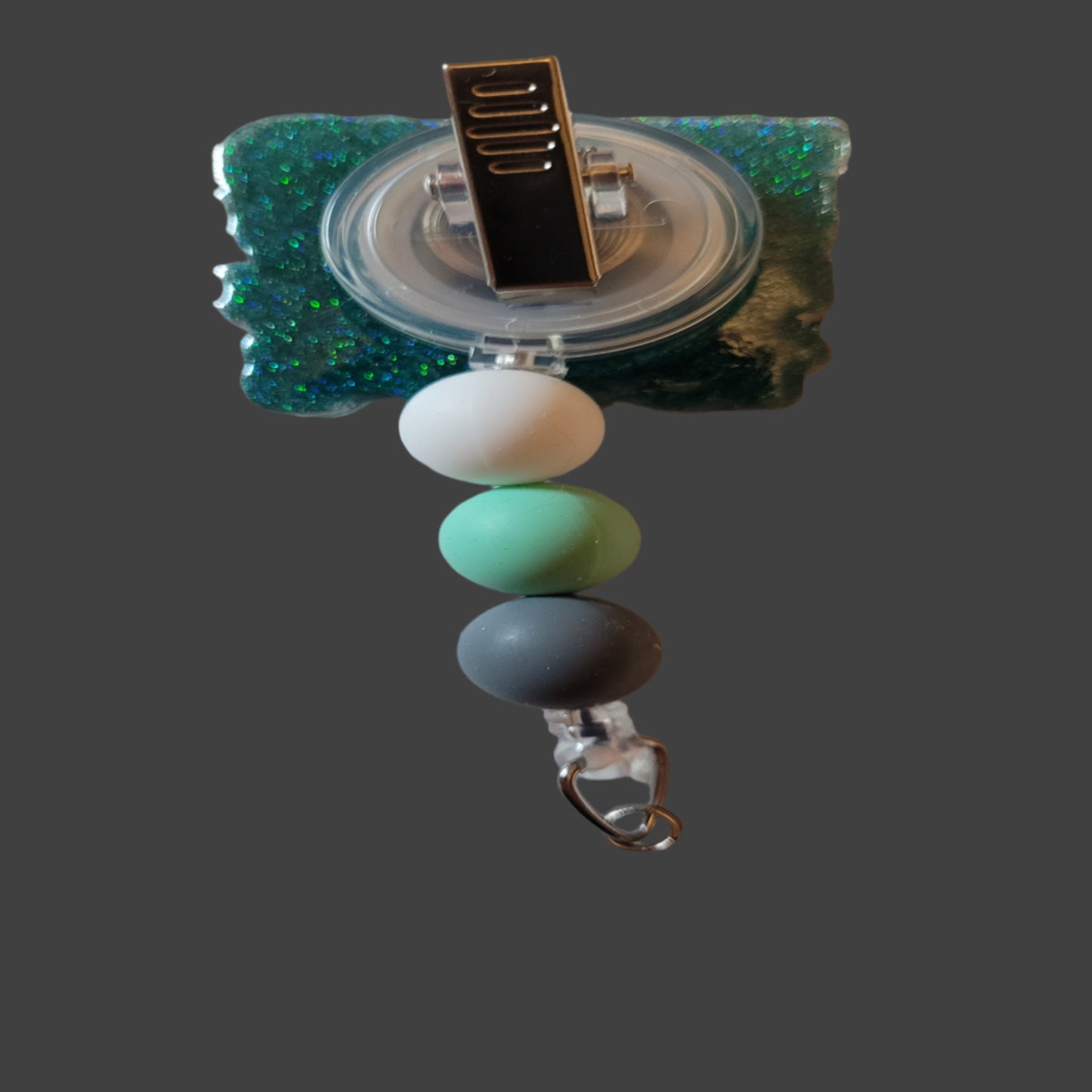 Get ready to travel back in time with this playful Badge Reel inspired by the 1900's! The front features a covered wagon, a nod to the Oregon Trail, and the catchy phrase "Please Be Patient With Me I'm From The 1900's". The back is a fun blue green glitter and is completed with 3 matching silicone beads.