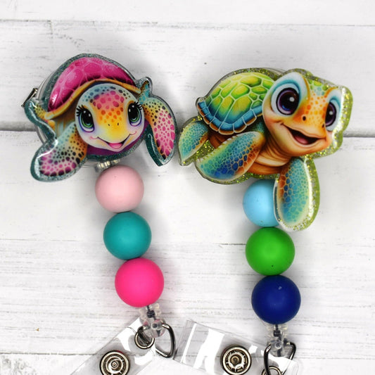 Animal enthusiasts will be delighted by these endearing pink and blue turtles in a badge reel, adorned with complementary beads for a polished look.