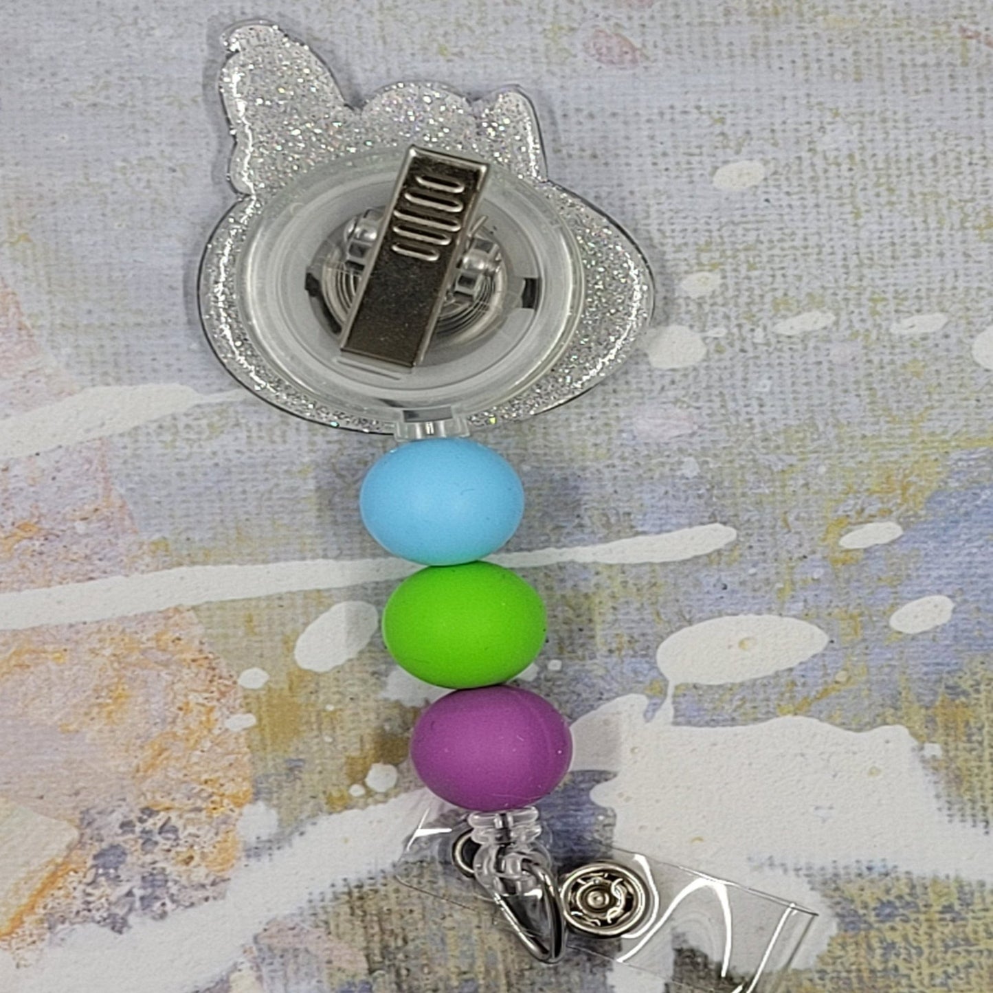 Everyone's Favorite Beagle has replaced is dog house with an Easter Egg as he takes his daily nap. Laying on a light blue egg with pink and green zig zag stripes on a clear glitter background and adorned with three perfectly matching silicone beads, adding a charming touch to this delightful accessory. A must-have for all animal enthusiasts!