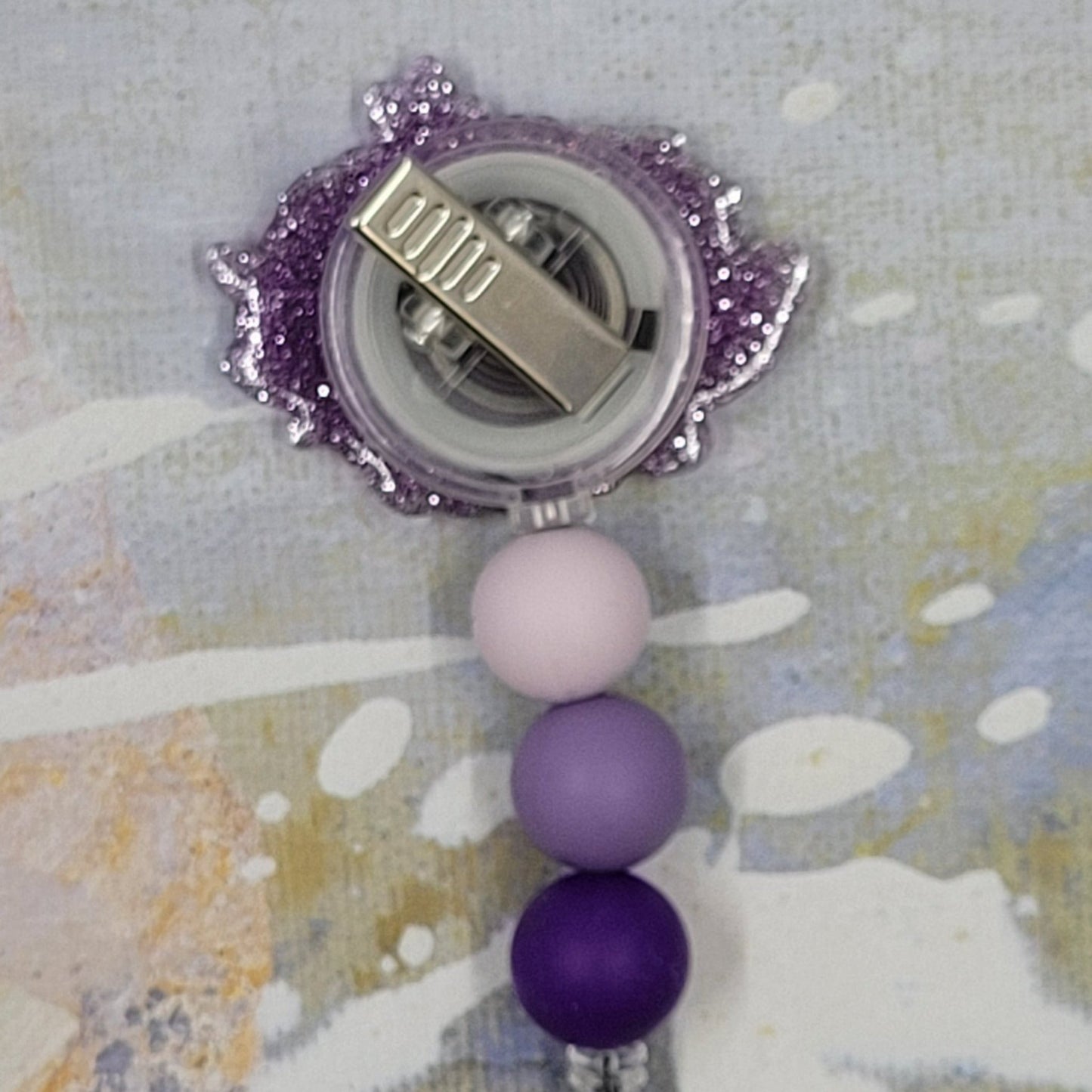 This Badge Reel features a cute purple floral hedgehog design paired with a shiny purple glitter background. The adorable hedgehog is complemented by three color-coordinated silicone beads for an extra touch of charm. Sure to be a hit with any animal lover.