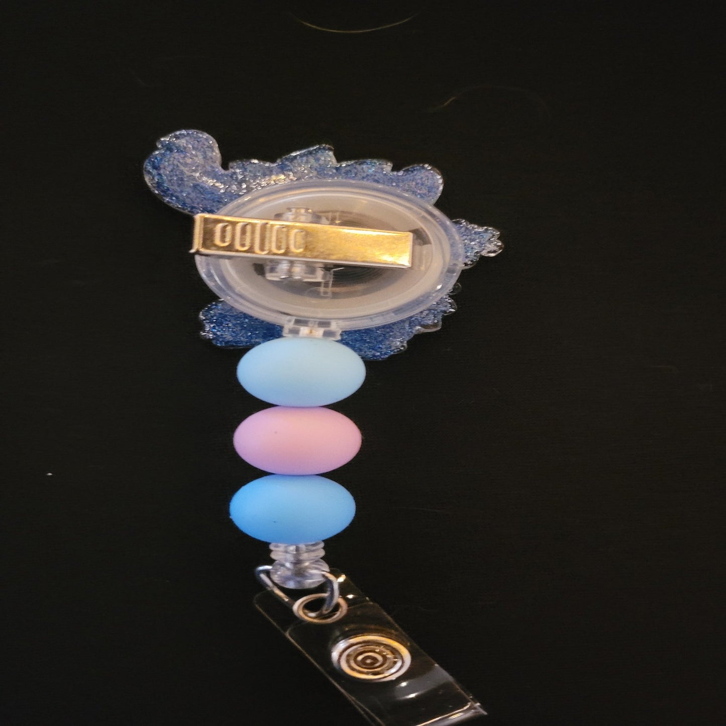 Stitch dancing a Hula in all his cuteness. This badge reel has a shiny glitter base and is finished with 3 color coordinated silicone beads.