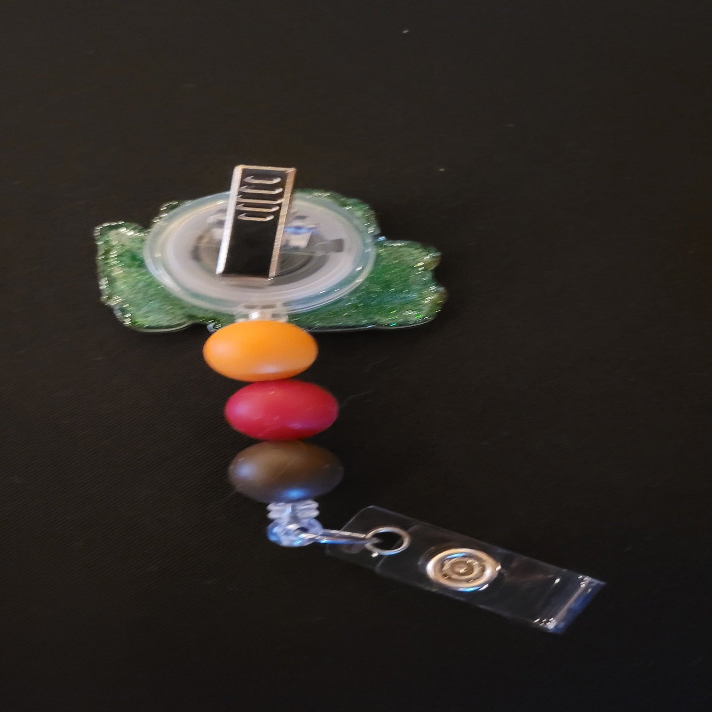 It's our favorite tow truck Mater. This iconic badge reel tow truck will be sure to pull you through the day. A shiny glitter base and is finished with 3 color coordinated silicone beads.