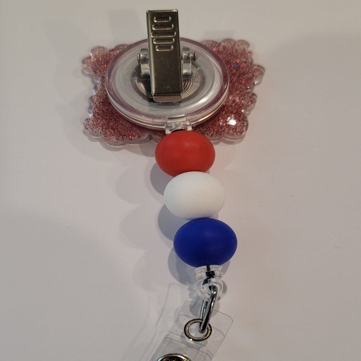 Oh My Stars & Stripes! Adding a touch of patriotism, this badge reel flaunts red, white, and blue silicone accent beads and a red glitter back. Perfect for showing your patriotism.
