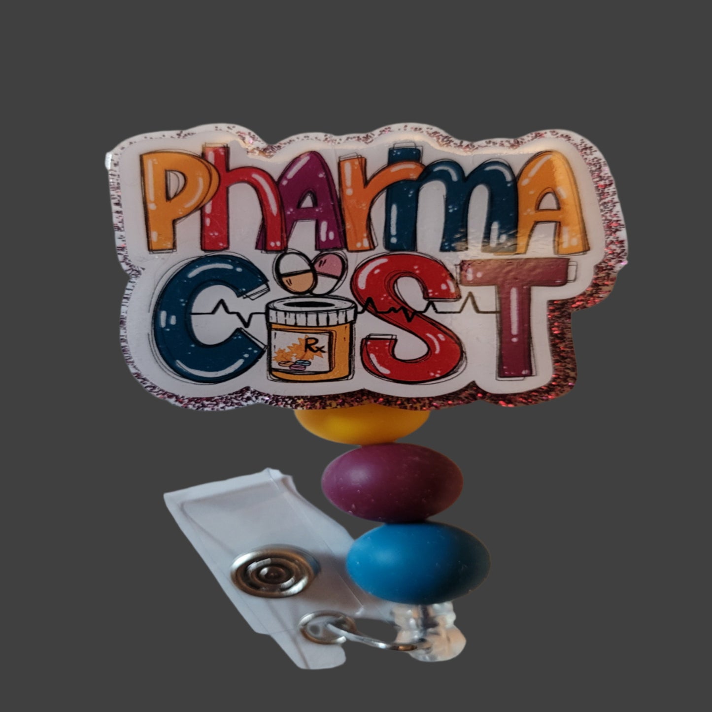 Introducing the Pharmacist Badge Reel - the newest addition to our Medical Badge Reel collection! With a playful font and color scheme featuring the word "Pharmacist", this reel is sure to catch some attention. Plus, the dark red glitter backing and 3 matching silicone beads add a touch of fun flair to complete the look.