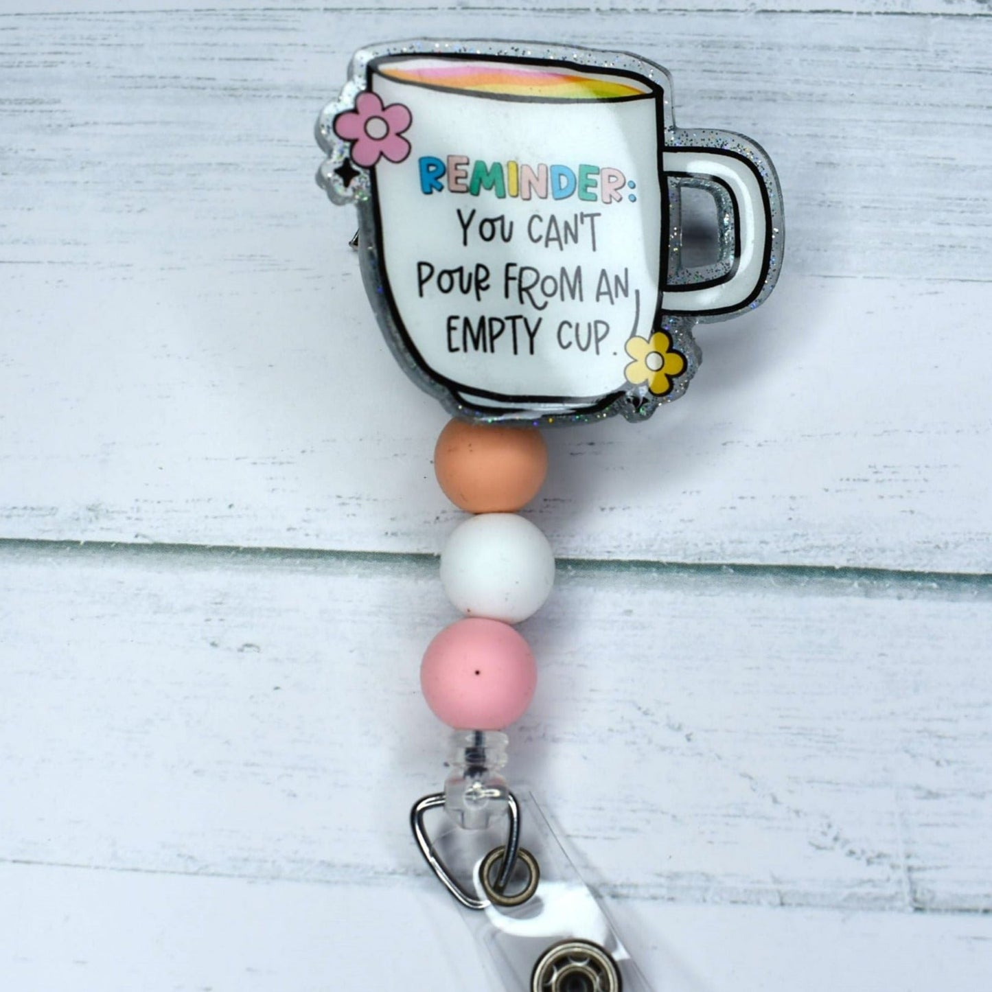 This acrylic badge reel features the motivating quote, "You Can't Pour From An Empty Cup," and is adorned with a peach white & pink silicone bead.