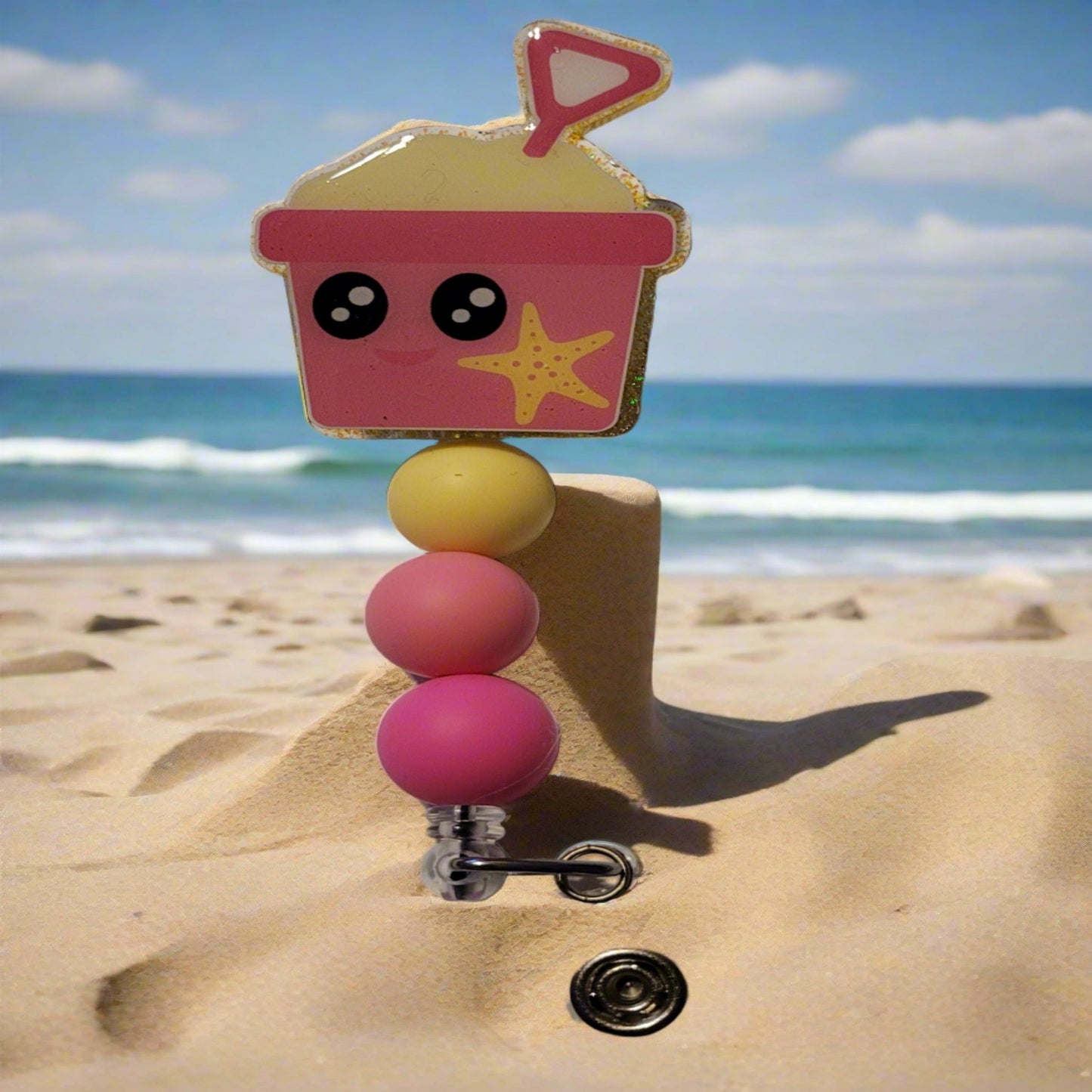 Heading to the beach? Grab your shovel & pail for some sandy fun! With a cheerful pink pail adorned with a bright yellow star fish and color-coordinated silicone beads to top it off.