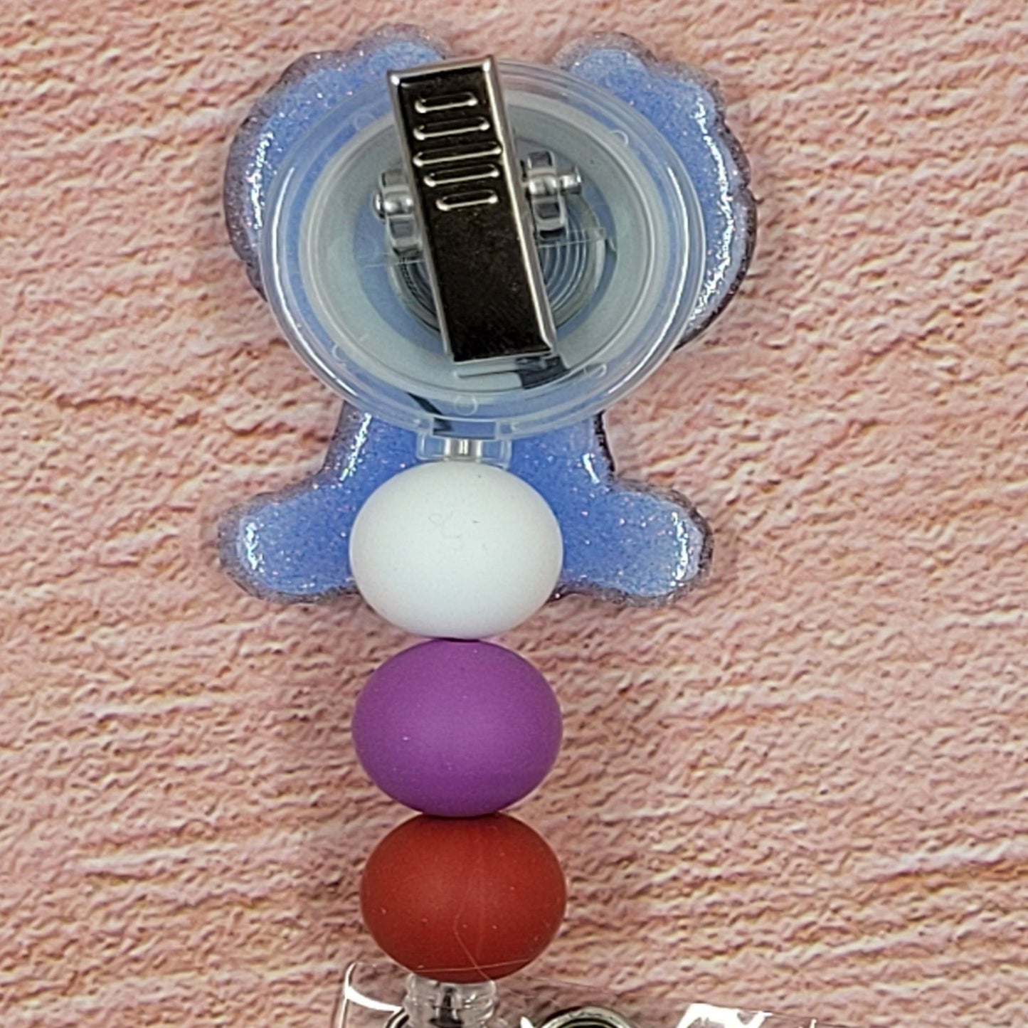 This badge reel features Experiment 626 asking you to be his Valentine. Wearing a cute head band with hearts and holding a big heart, this cute lil feller is adorable. A blue glitter base and 3 color coordinated beads finish the look..