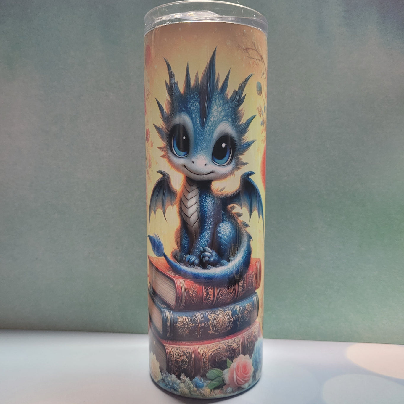 Introducing our latest addition The Dragon Series. Here Be Dragons. We call this one Baby Book Dragon. No fierce looking eyes, thunderous roars or fire breathing from this little one. This cute blue dragon with it's big blue eyes sits atop 3 books and is surrounded by candles and roses. This is made from stainless steel with a double-wall construction and is vacuum insulated, with a clear sliding classic lid and a clear straw, and is BPA free.