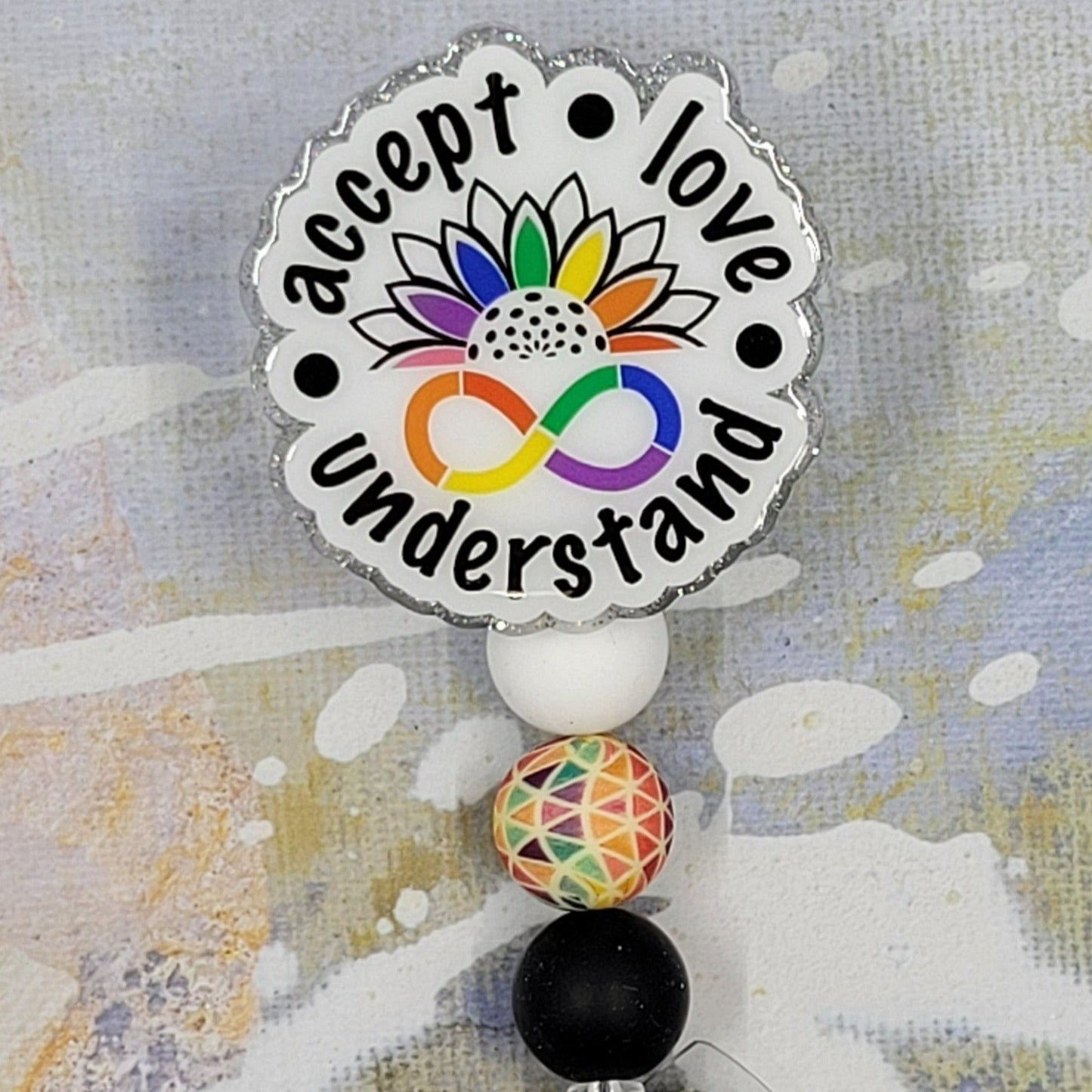 This badge reel, featuring the phrase "Accept Love Understand", aims to promote inclusivity across all backgrounds. It has a clear base with a glitter finish and is adorned with three coordinating silicone beads