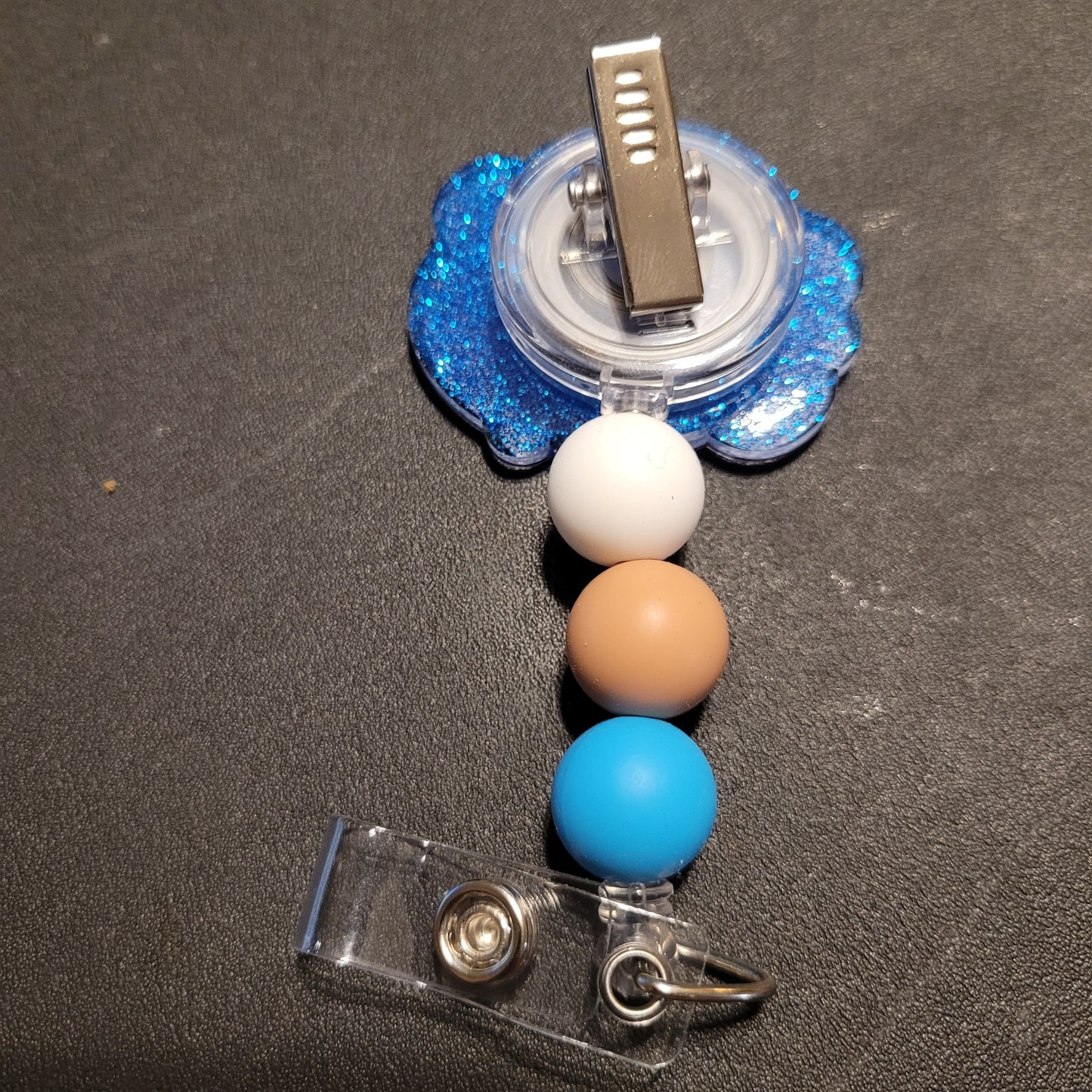 Retractable badge holder with blue, white, and brown beads on a dark surface