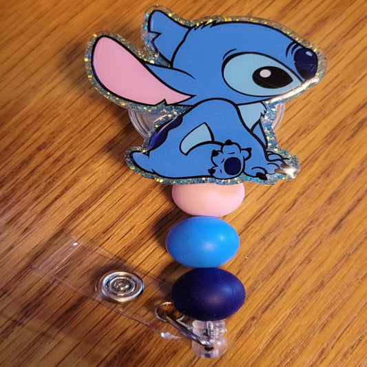 Everyone's favorite little blue alien dog is here and sitting like a good boy. A dazzling blue glitter backing and 3 color-coordinated silicone beads add the perfect finishing touch to this out-of-this-world badge reel.