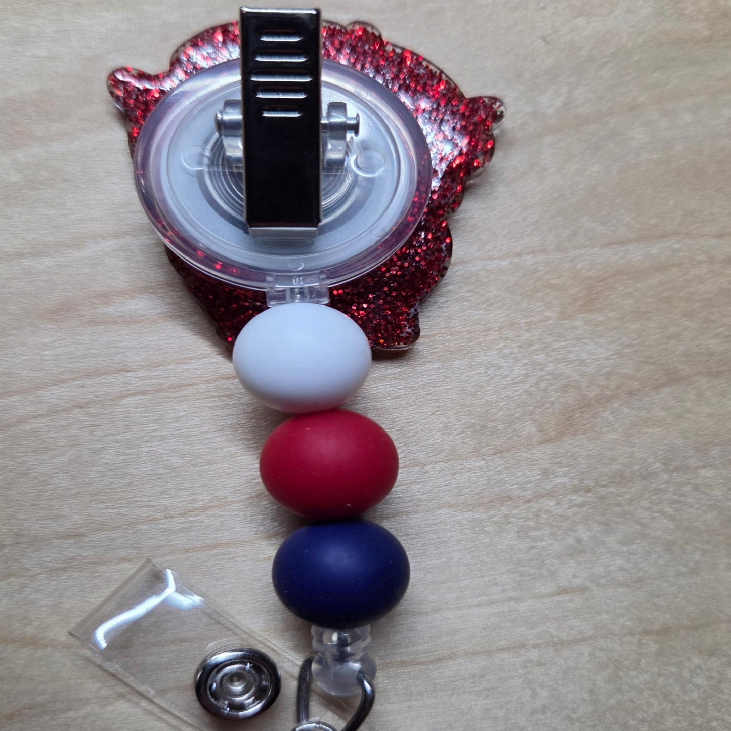 Red, white, and blue beaded badge holder with a clear plastic clip on a wooden surface.