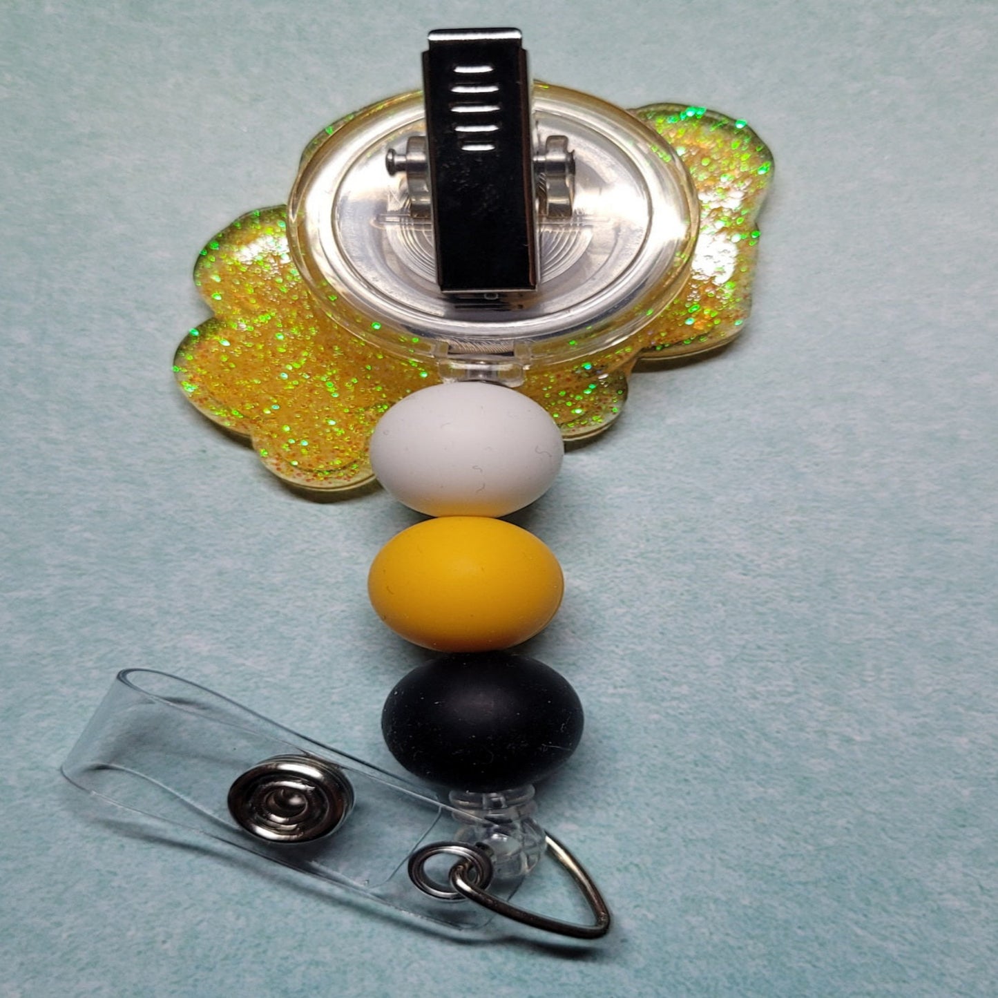 Emoji Nurse has a cute smiling freckle fac, stethoscope in 1 hand and an iced tea in the other ready to help those in need. Decked out in a sparkling green glitter back and embellished with 3 silicone beads.
