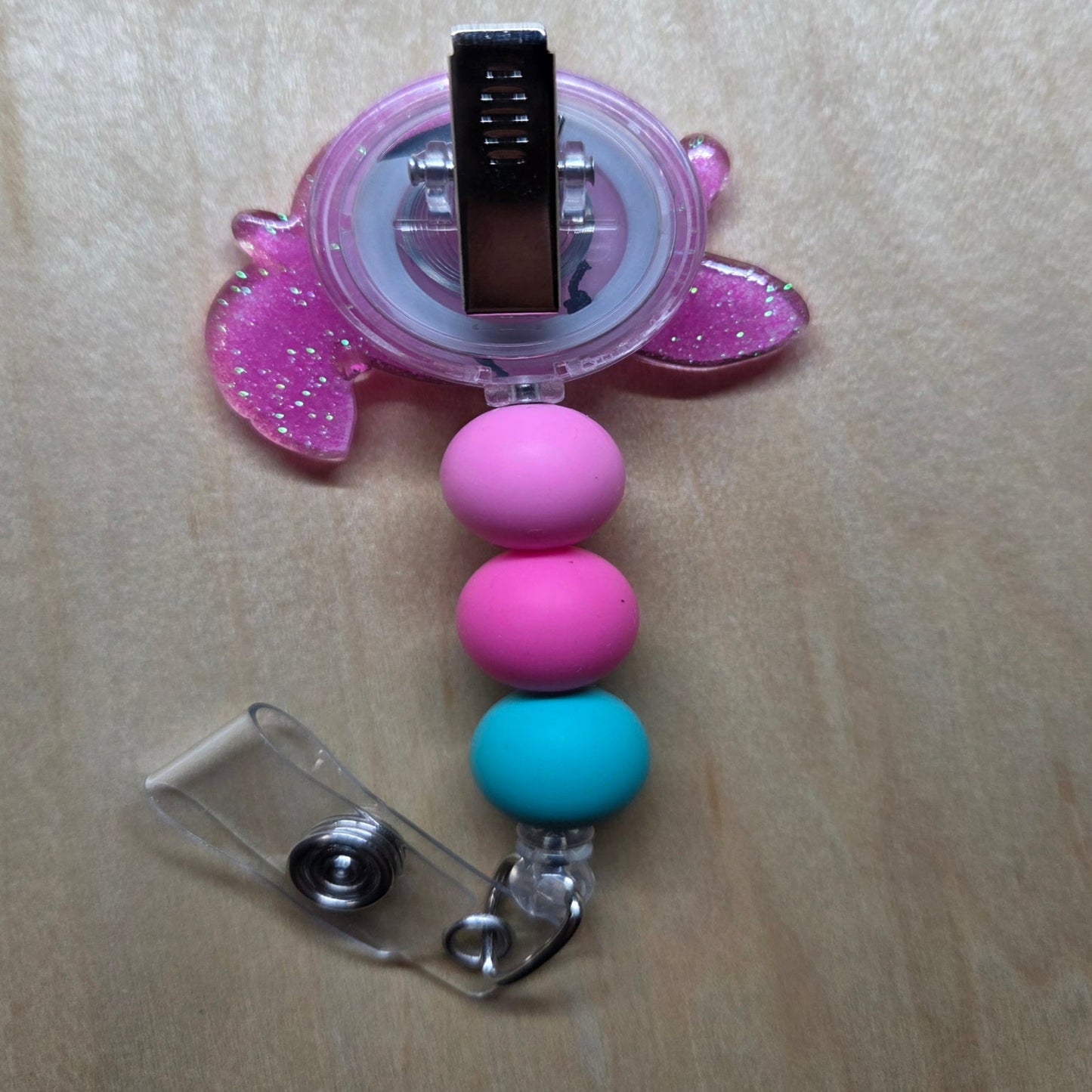Pink and blue beaded badge holder with a clip on a light wooden surface