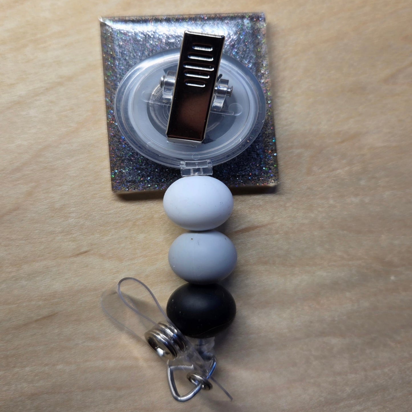 Retractable badge holder with black and white beads on a wooden surface