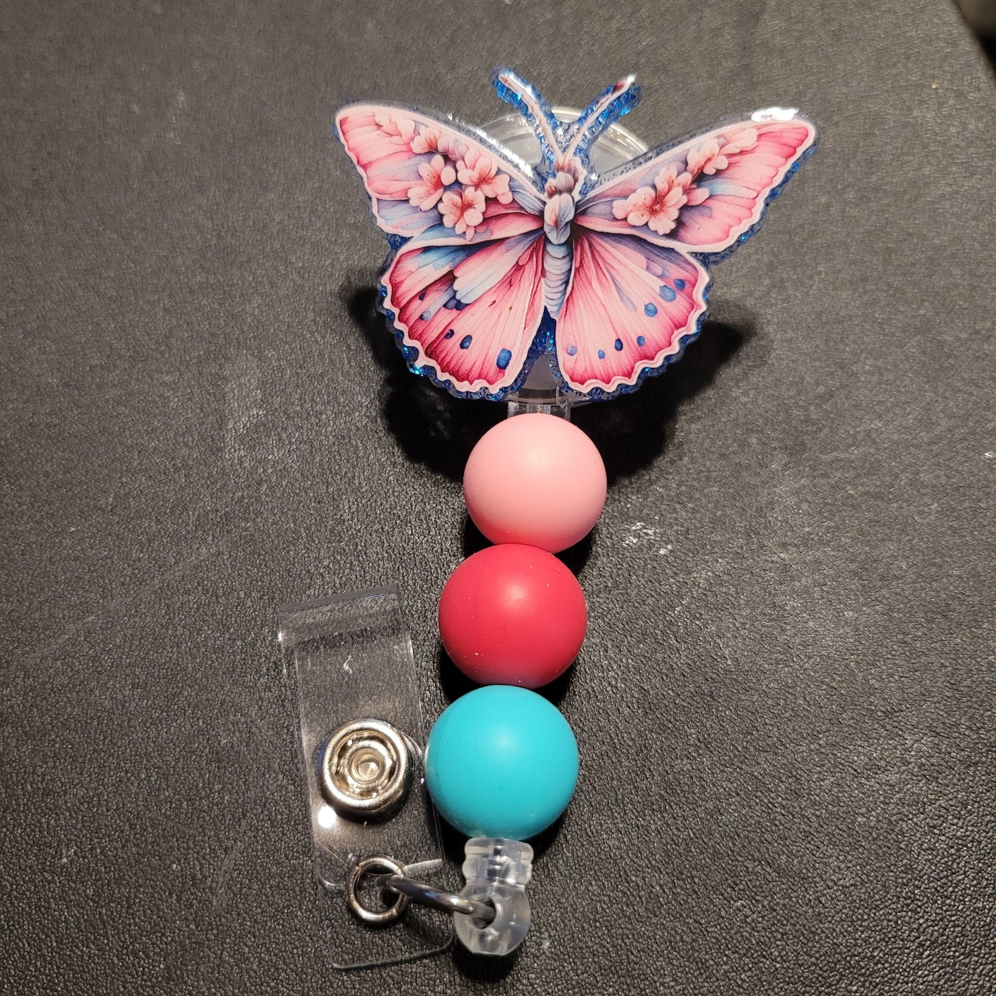 Butterfly-themed badge holder with colorful beads on a dark surface