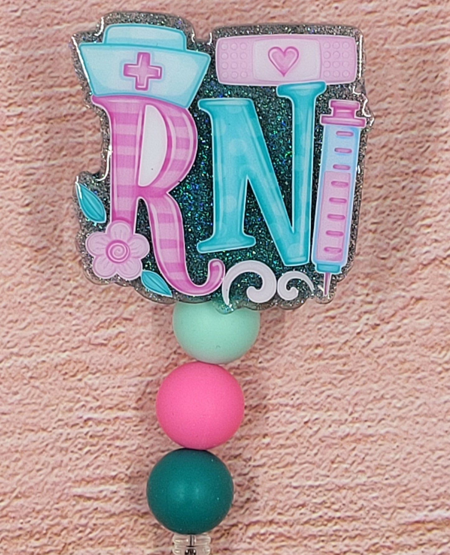 Introducing the new RN Badge Reel, part of our latest collection of Medical Badge Reels available now. Featuring a blue glitter base adorned with coordinating beads in shades of pink and blue, this Badge Reel is sure to catch the eye.