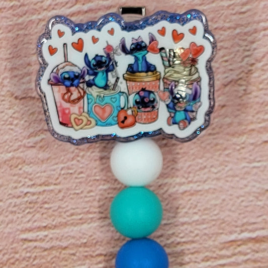 The Badge Reel Alien Drink Party showcases a group of 626s indulging in their preferred beverages. The elegant design is enhanced by a sparkling blue base and three color-coordinated beads.