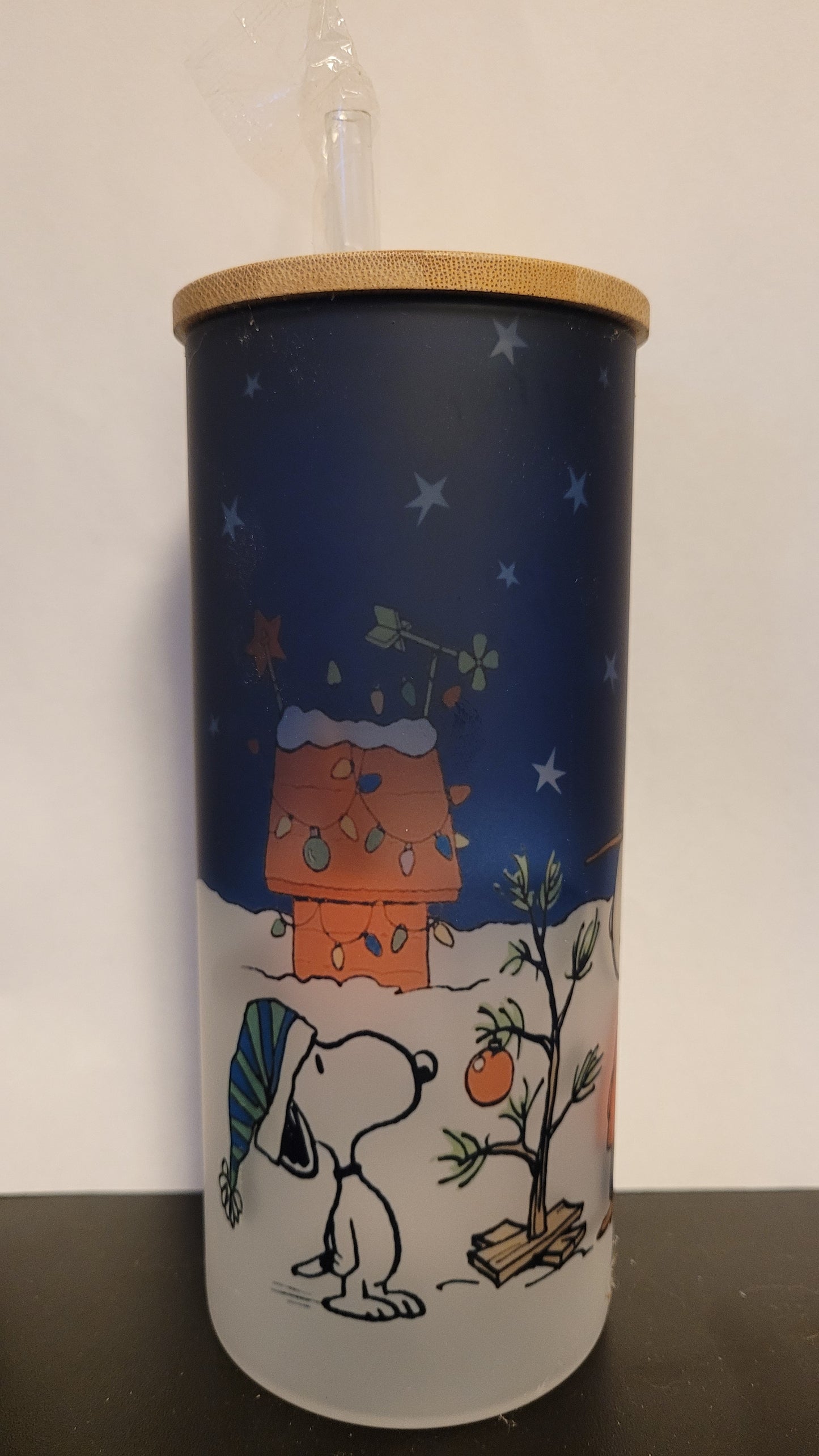 It's a Peanuts Christmas. Charlie Brown & Snoopy stand outside admiring the iconic Charlie Brown Tree. This image is sublimated onto a glass can tumbler and comes with a straw and bamboo lid.