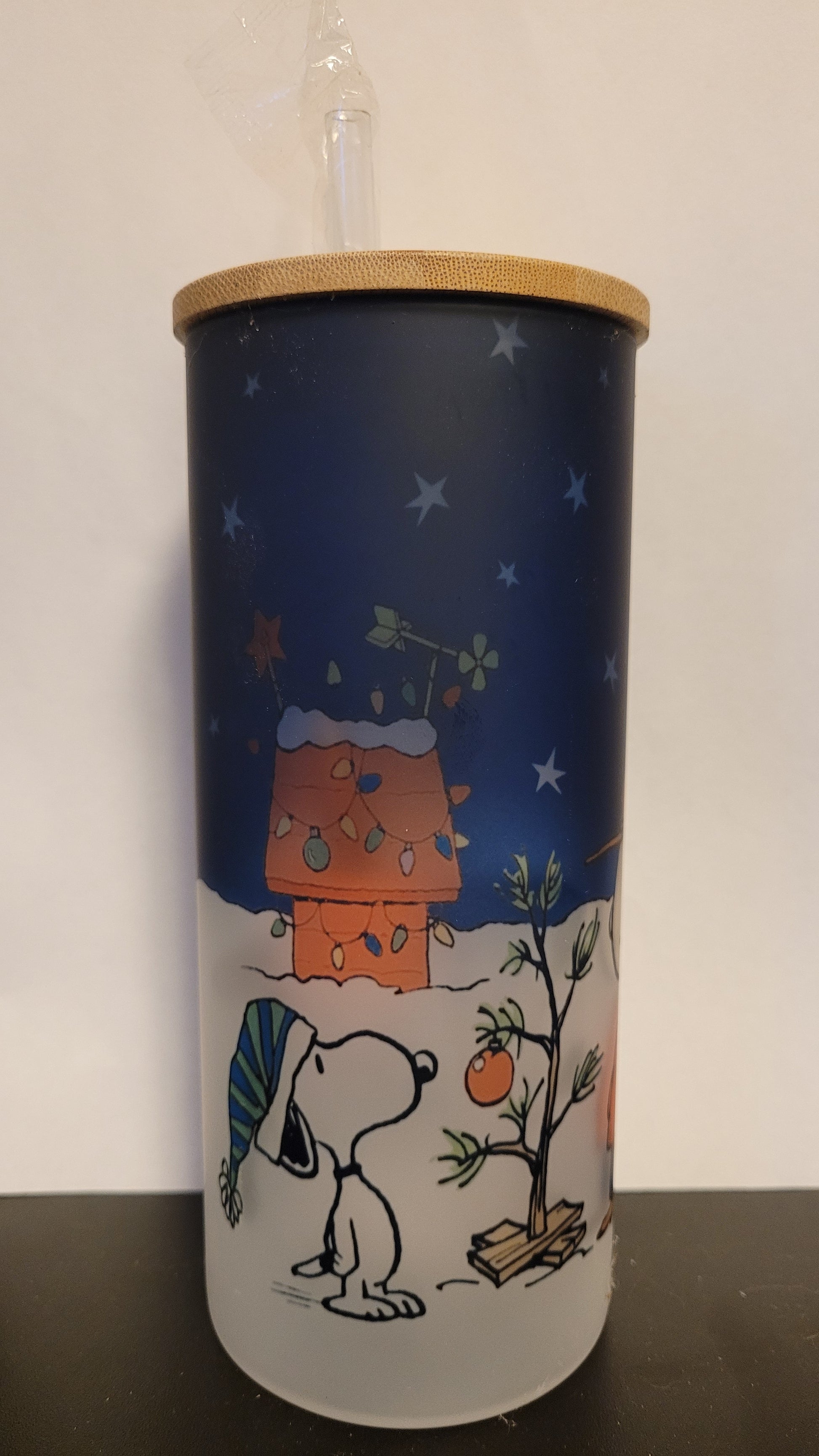 It's a Peanuts Christmas. Charlie Brown & Snoopy stand outside admiring the iconic Charlie Brown Tree. This image is sublimated onto a glass can tumbler and comes with a straw and bamboo lid.