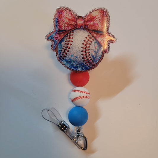 Decorative keychain with baseball design and colorful bow on a plain background