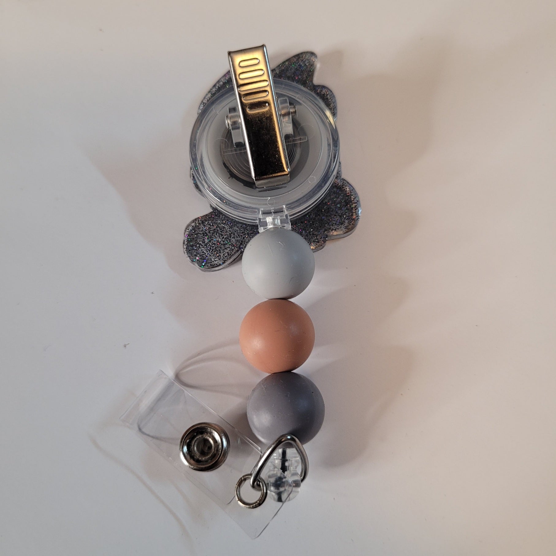 Clear holder with colorful beads and a gold clip on a light background