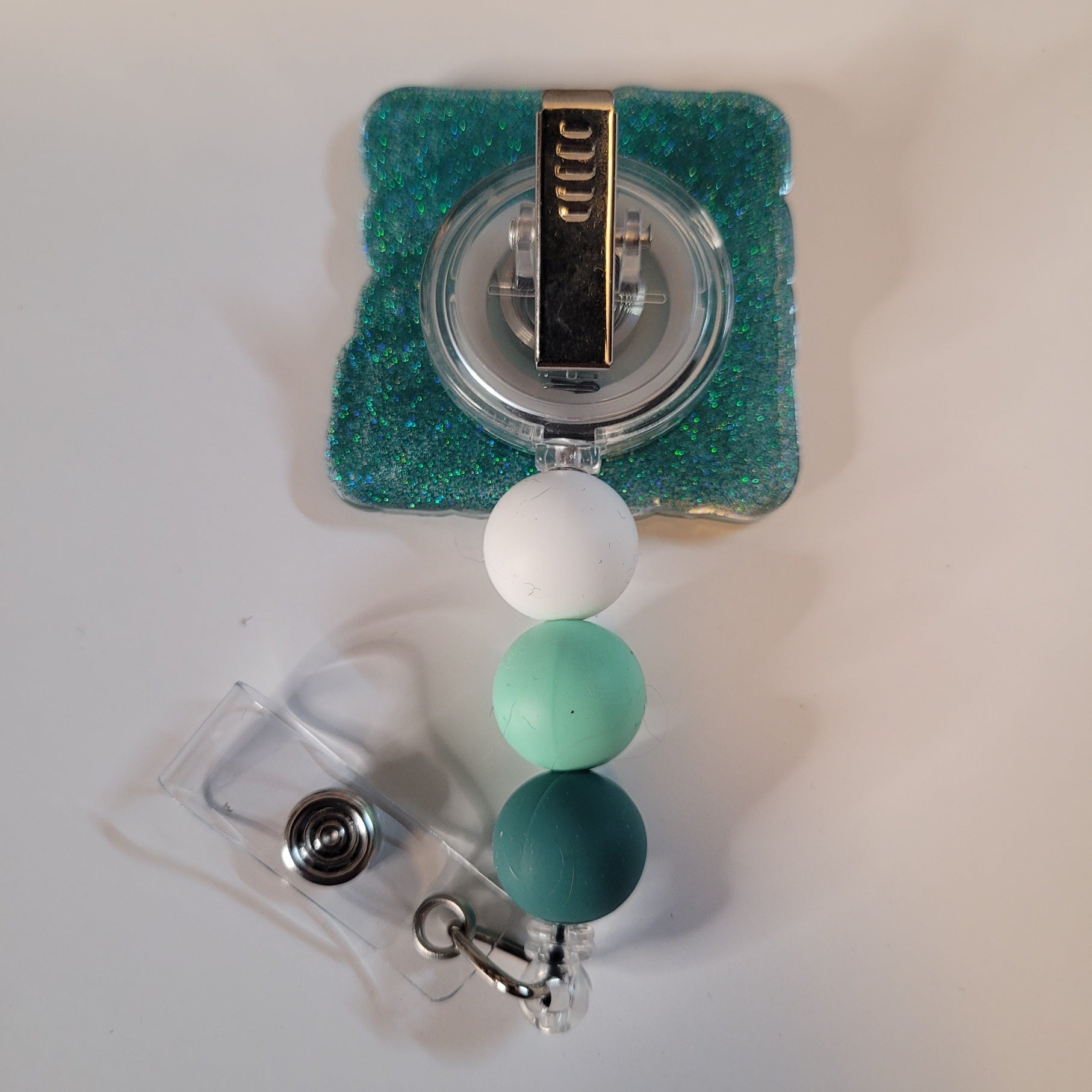 Green and white beaded badge holder with a clear plastic clip on a light gray background