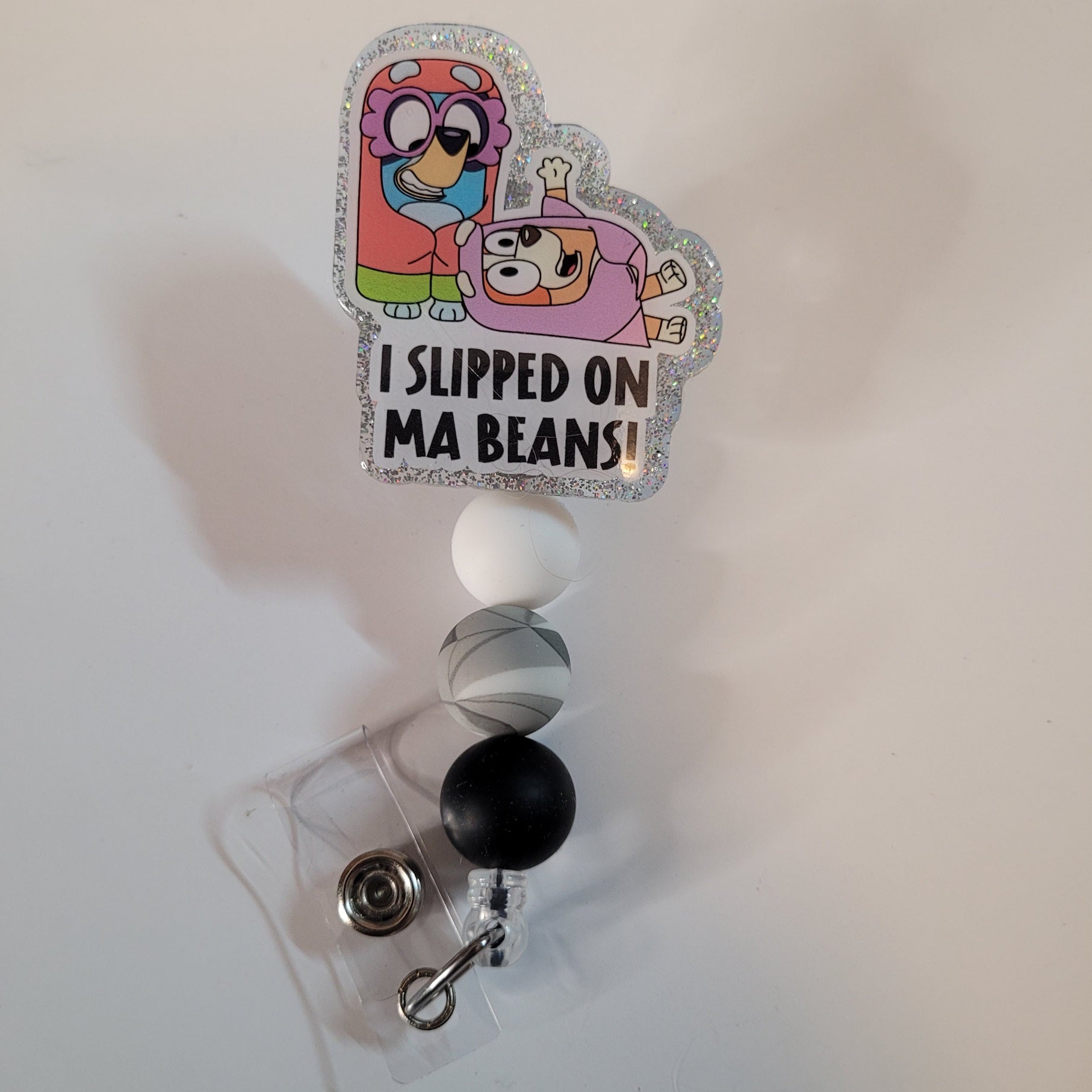 Retractable badge holder with cartoon characters and text 'I Slipped on Ma Beans!' on a white background