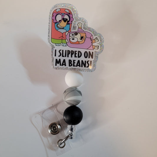 Retractable badge holder with cartoon characters and text 'I Slipped on Ma Beans!' on a white background