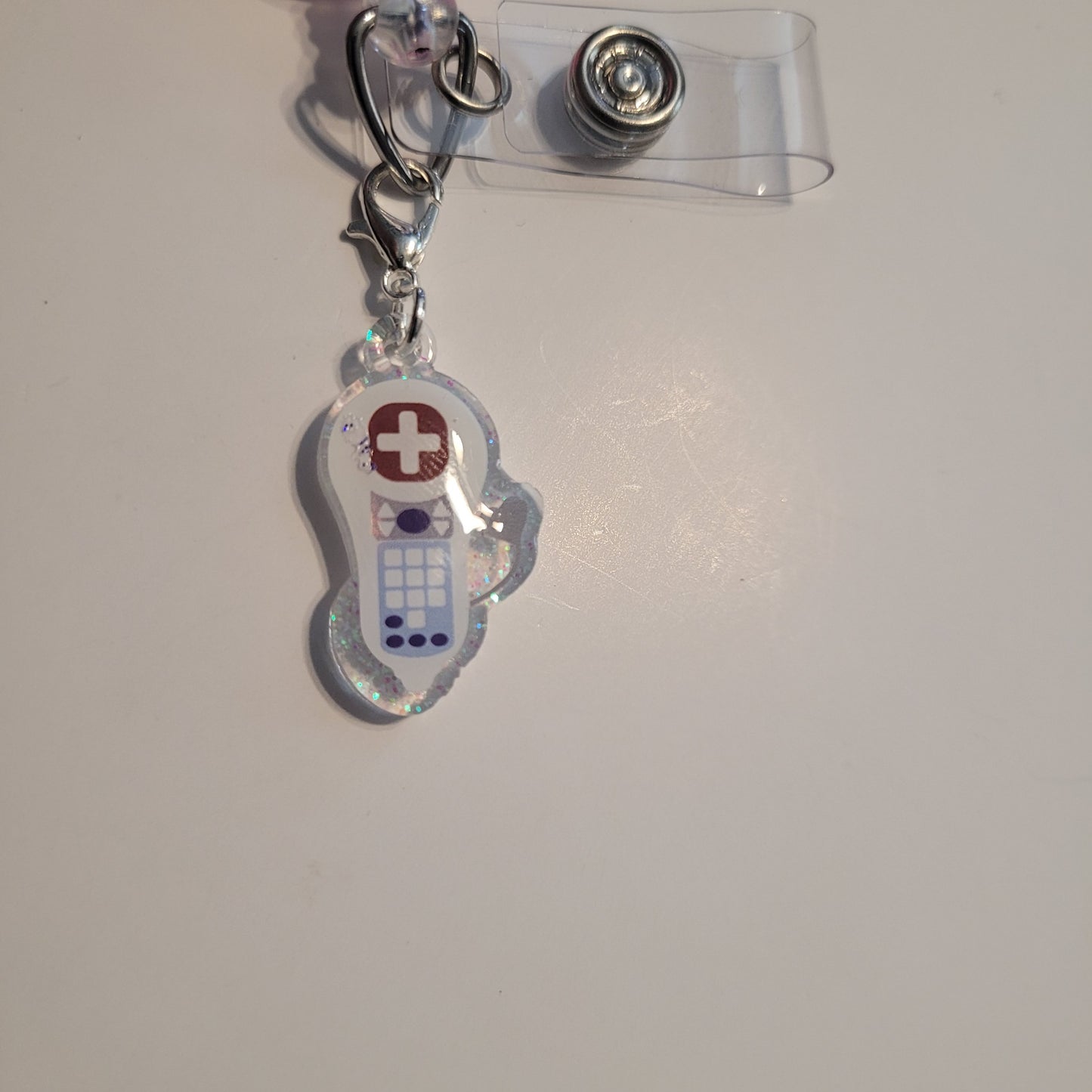 Clear badge holder with a small charm featuring a medical cross on a white background