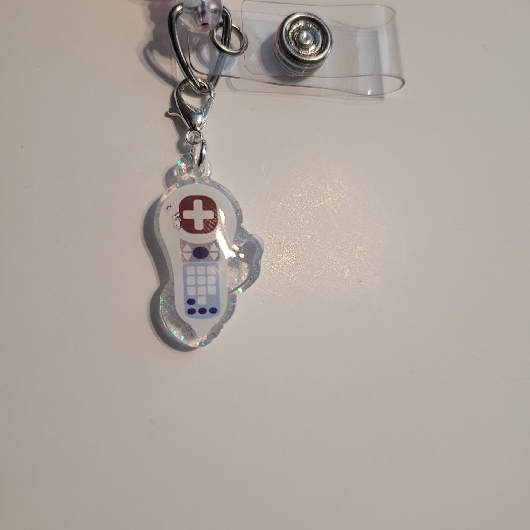 Clear badge holder with a small charm featuring a medical cross on a white background