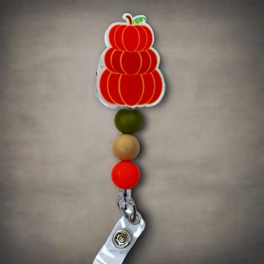 This acrylic badge reel features  3 pumpkins stacked with a green tan and orange silicone bead for the finishing touch