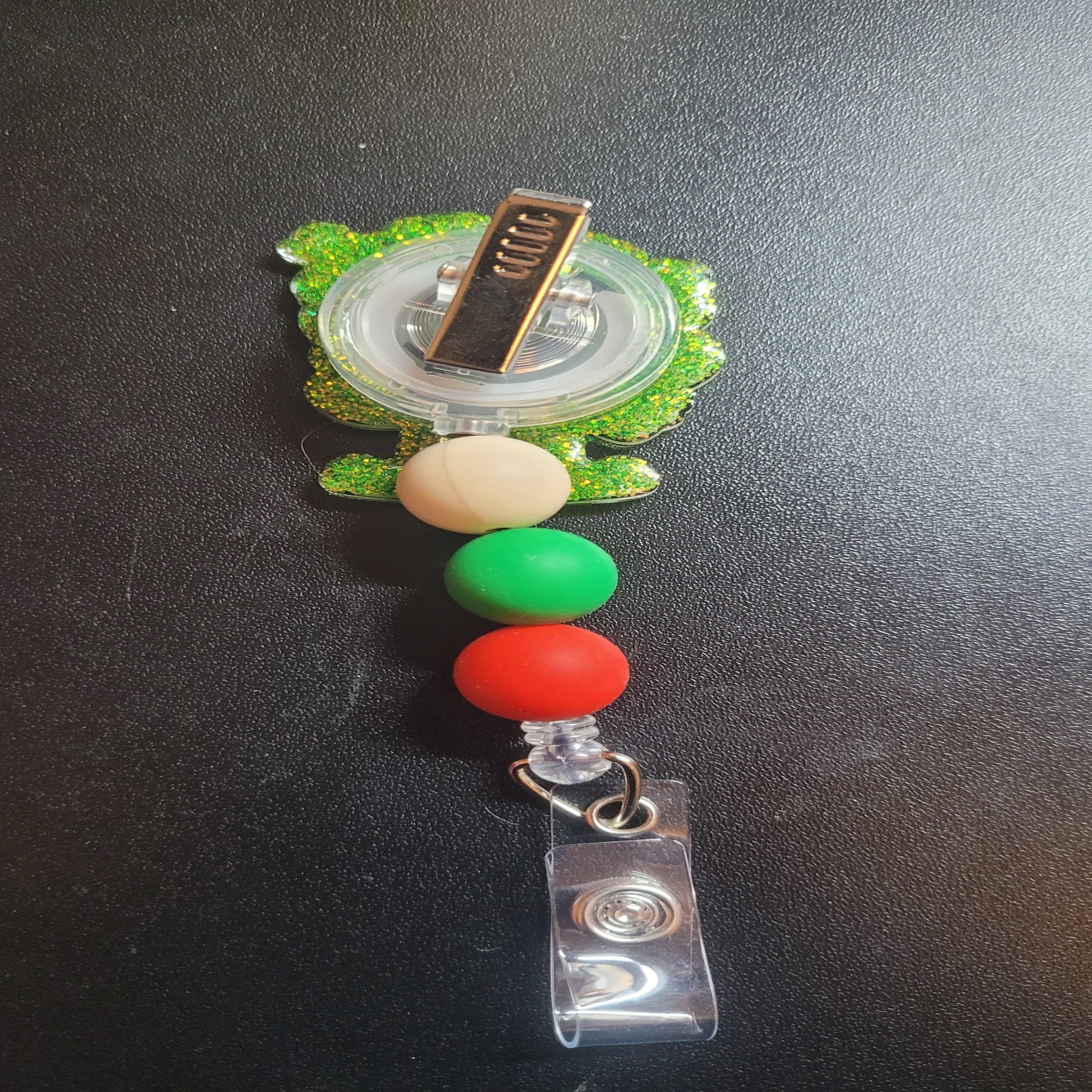 I'm The Chatty Elf badge reel is here for all to talk about. A fun elf clothing image with multiple Bla Bla Bla word clouds floating around. Features a green glitter back and 3 color coordinated silicone beads.