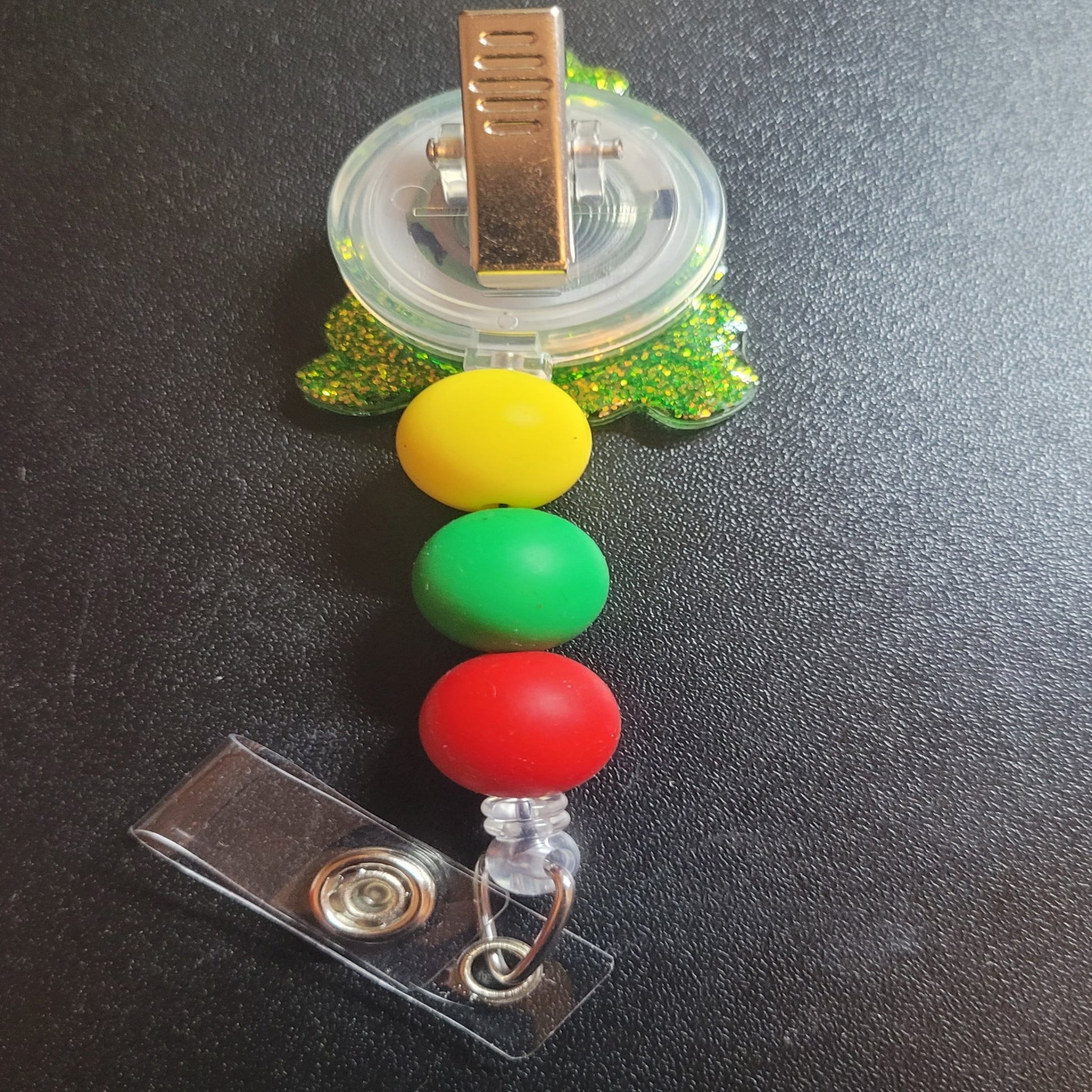 Tis the season for the lighting of the Christmas Tree. This badge reel makes a festive addition to your look with red ornaments, a gold glitter background and 3 silicone accent beads. Ideal for celebrating the Christmas Holidays.