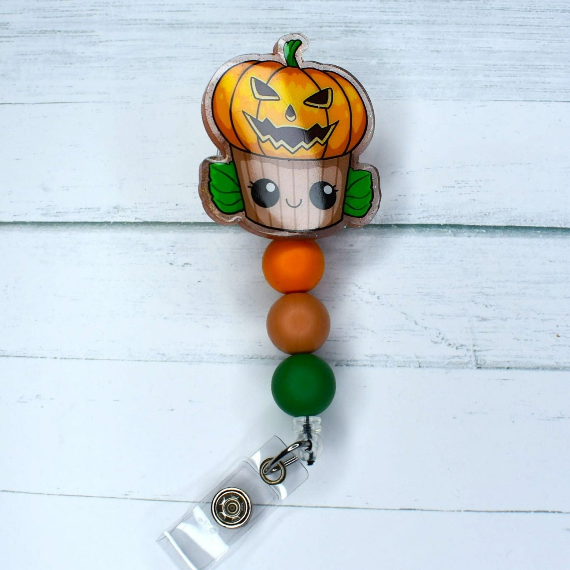 Here we have a scary cupcake Jack-o-Lantern acrylic badge reel featuring orange light salmon & green silicone beads. 