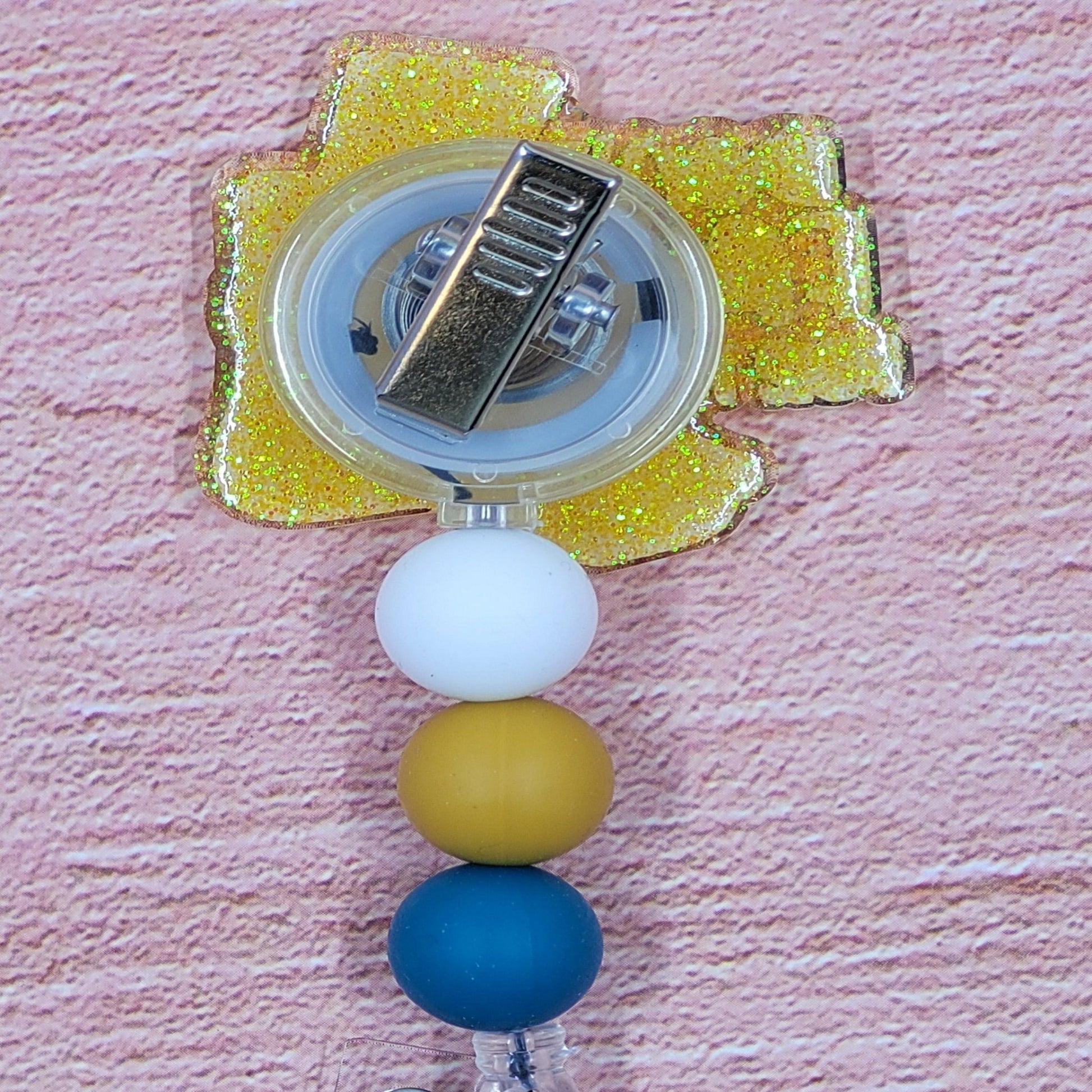 If you have ever spent any time as a patient in a hospital...you know what these are....GRIPPY SOCKS. So warm and comforting and all those rubber grips to help keep you from falling! This badge reel depicts those socks with a yellow glitter base. The phrase Don't Fall For Me in blue lettering and 3 color coordinated silicone beads.