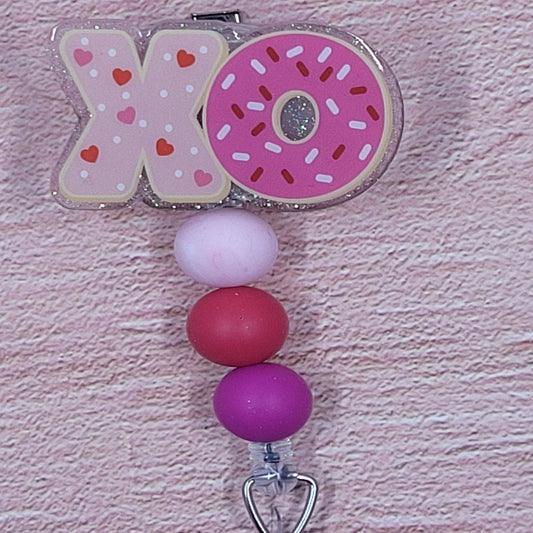 XOXOXO Here we present to you our new Hugs & Kisses Badge Reel. What would Valentine's Day be without them! Featuring a light pink glitter base and coordinated beads, this is the perfect accessory for the holiday season.