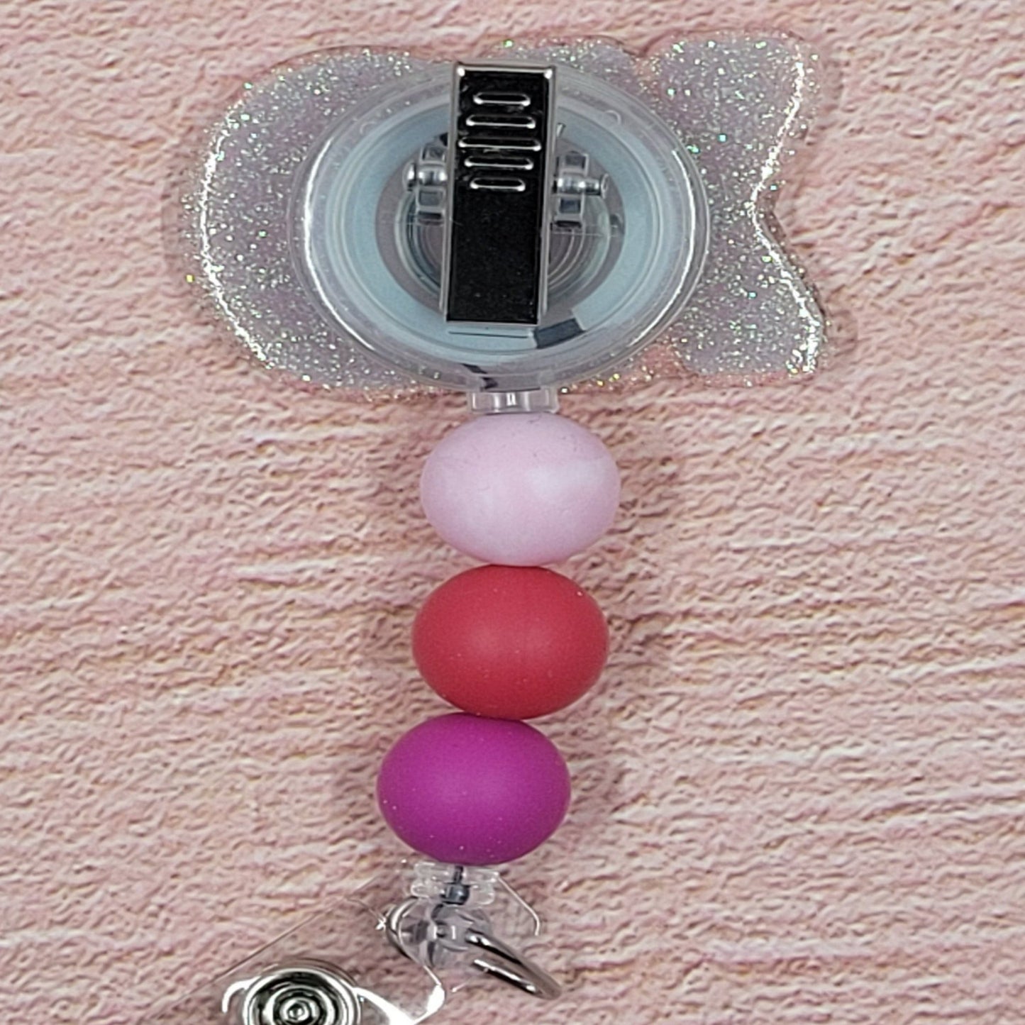 XOXOXO Here we present to you our new Hugs & Kisses Badge Reel. What would Valentine's Day be without them! Featuring a light pink glitter base and coordinated beads, this is the perfect accessory for the holiday season.
