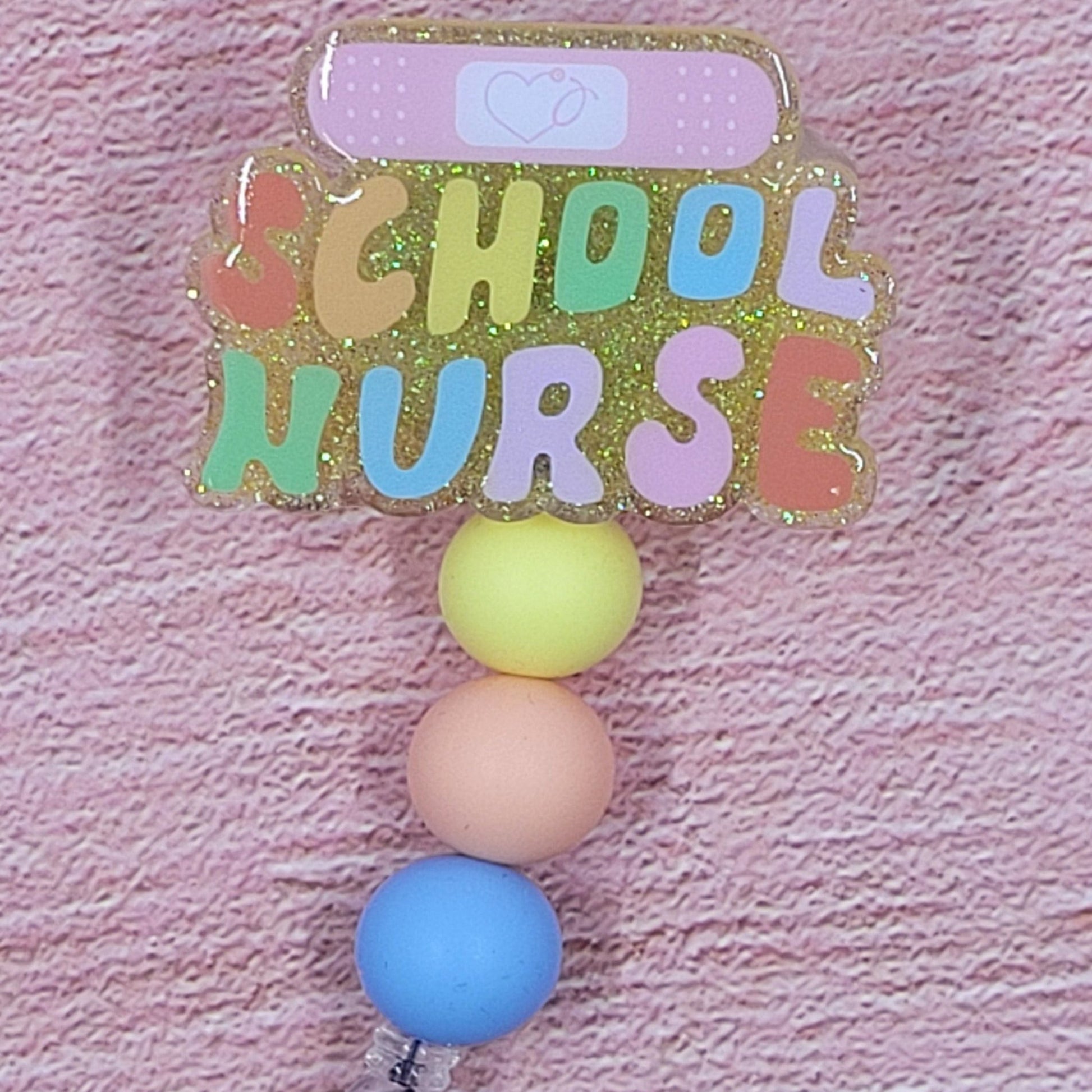 Introducing the new School Nurse Badge Reel, part of our latest collection of Medical Badge Reels available now. Featuring School Nurse with a Band-Aid and a yellow glitter base adorned with coordinating beads, this Badge Reel is sure to catch the eye.
