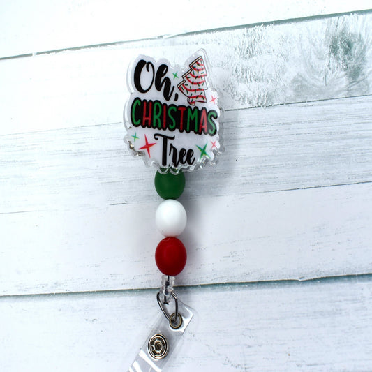 This acrylic badge reel proudly displays a classic holiday treat - the Christmas Tree Snack cake. A white background and festive-hued silicone beads complete this seasonal delight, which is tastefully adorned with the words "Oh Christmas Tree".